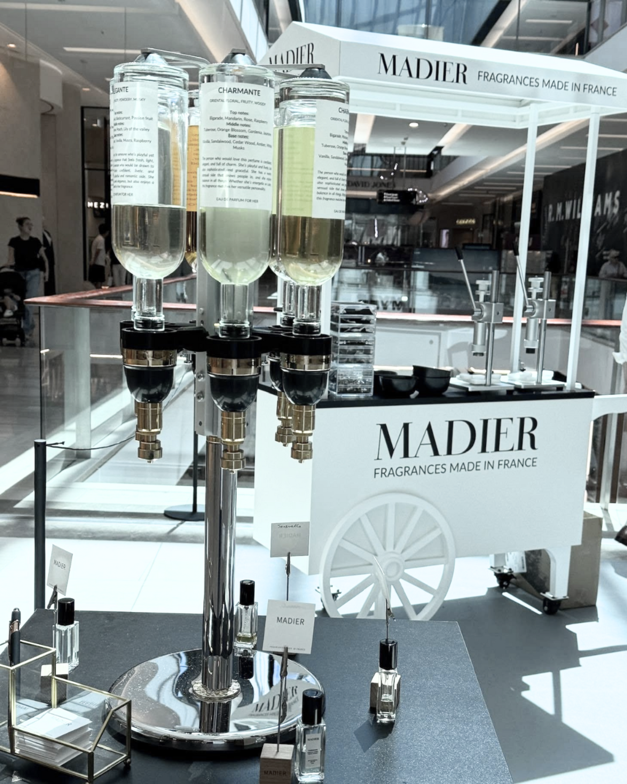 Modern fragrance cart with glass perfume dispensers and bottles displayed in a shopping mall.