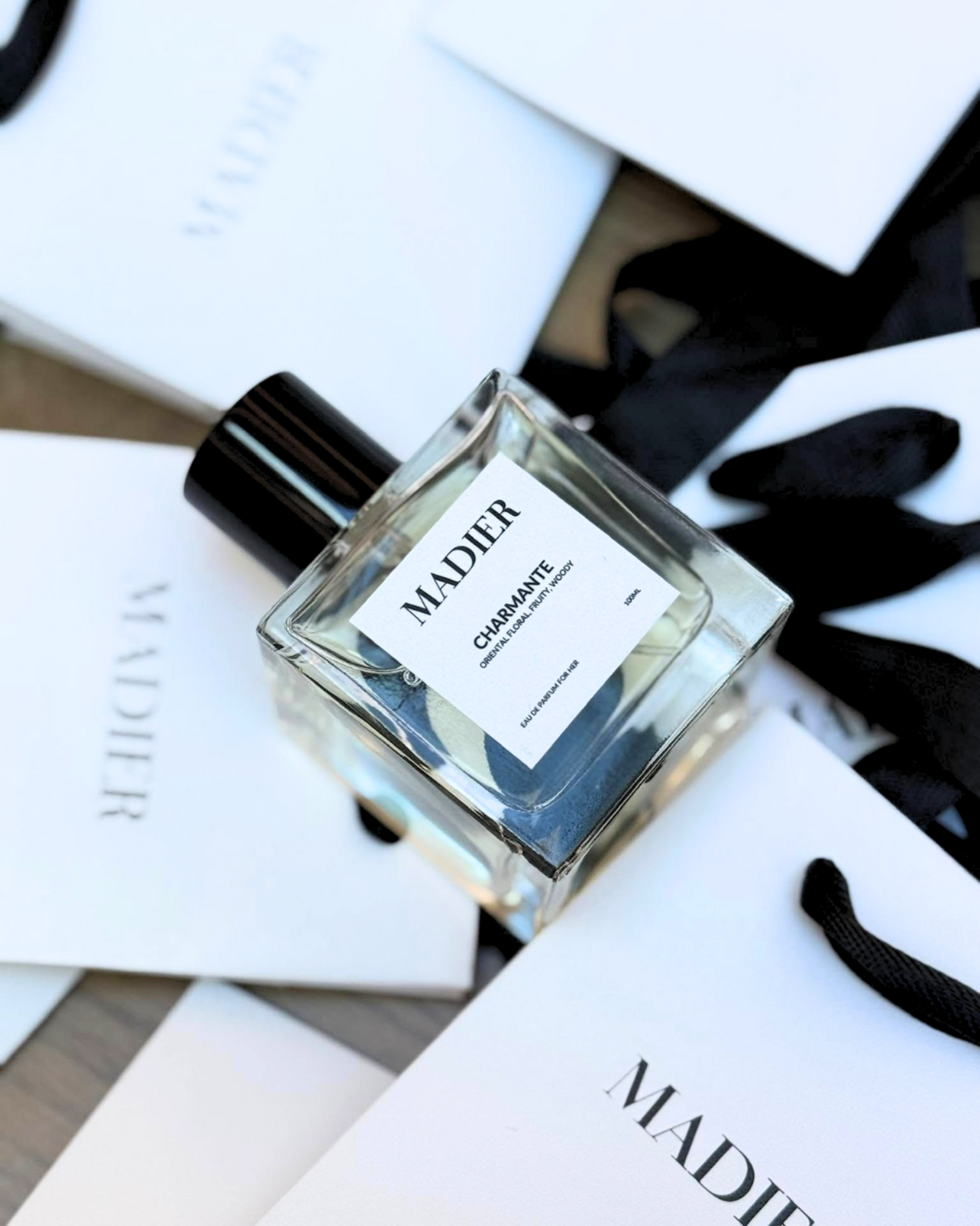 Minimalist flatlay of a MADIER perfume bottle styled with white cards and black ribbons for a wedding.