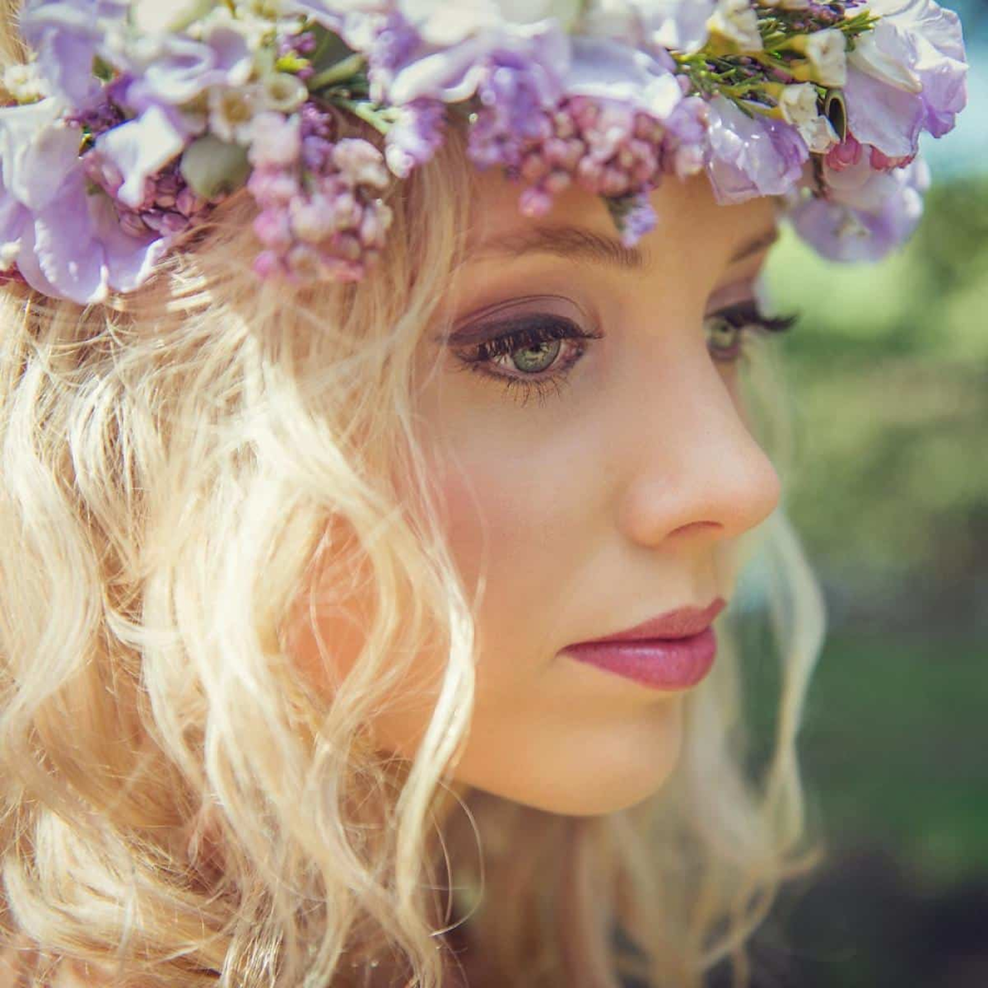 Close-up bridal portrait with a purple flower crown and soft natural makeup in outdoor light