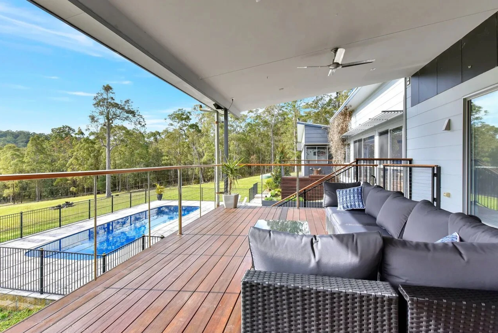 Modern country home deck overlooking a pool and expansive green grounds surrounded by trees.