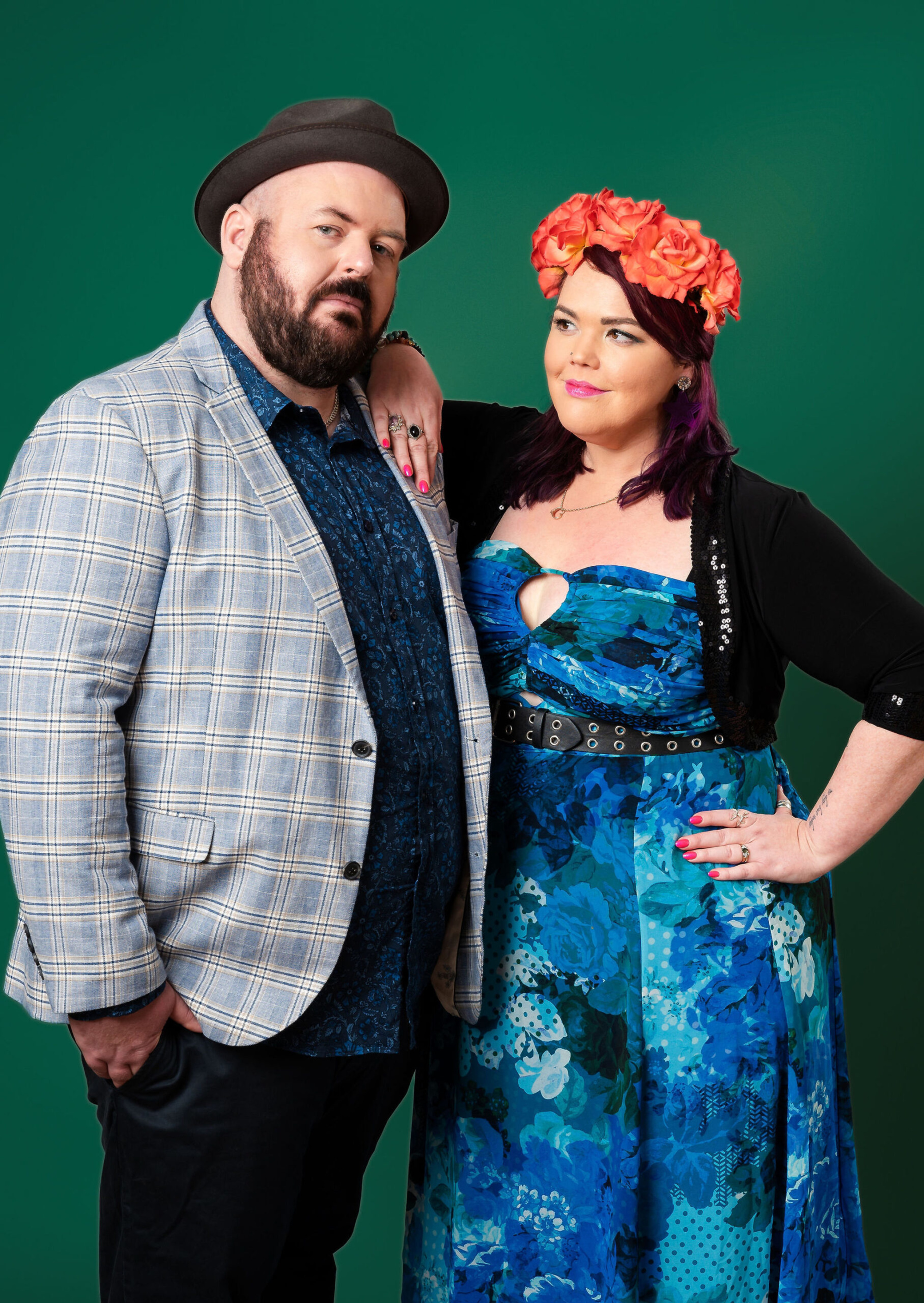 Colorful portrait of a stylish couple standing together against a green backdrop.