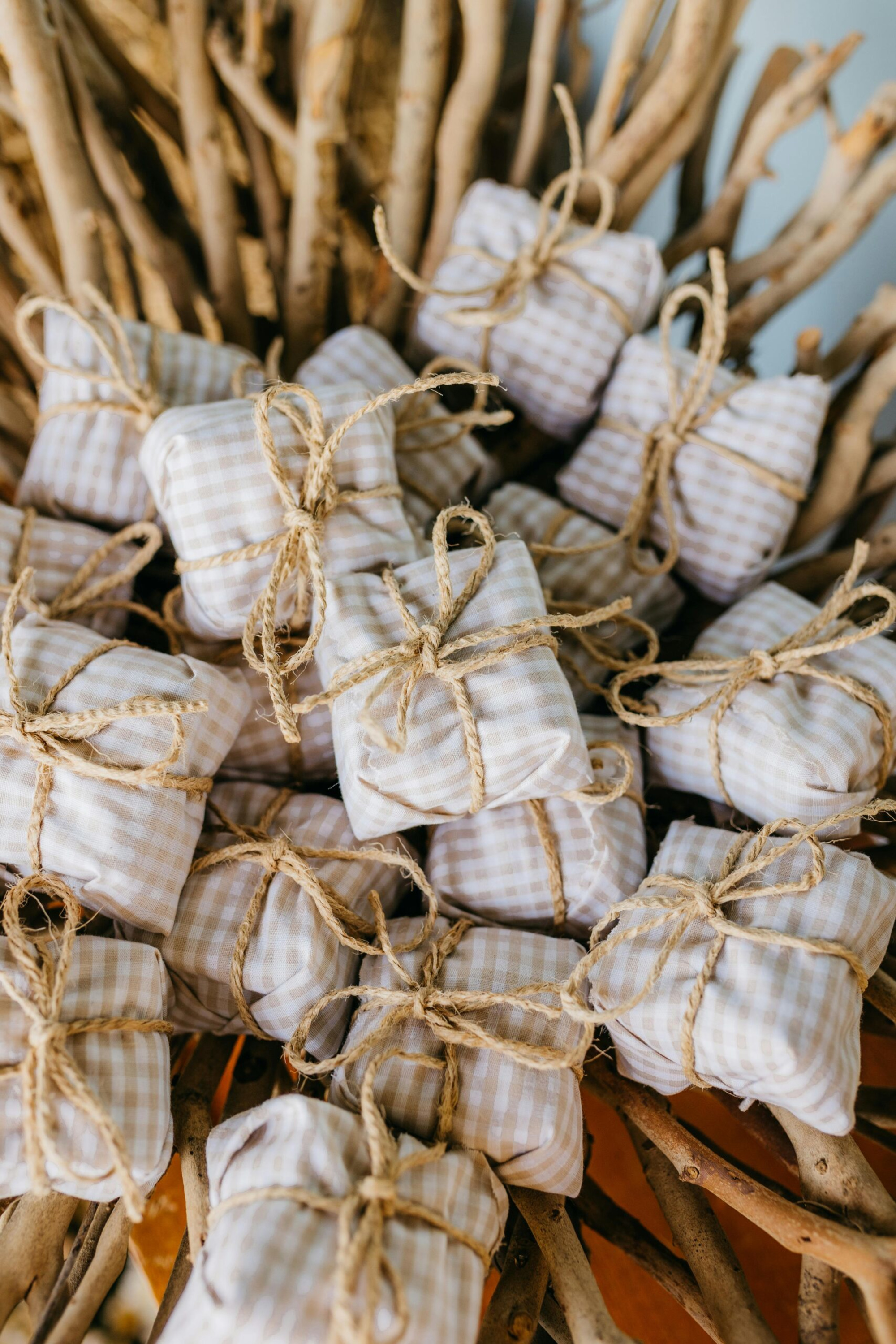 Small gingham-wrapped wedding favors tied with twine displayed on rustic wooden branches.