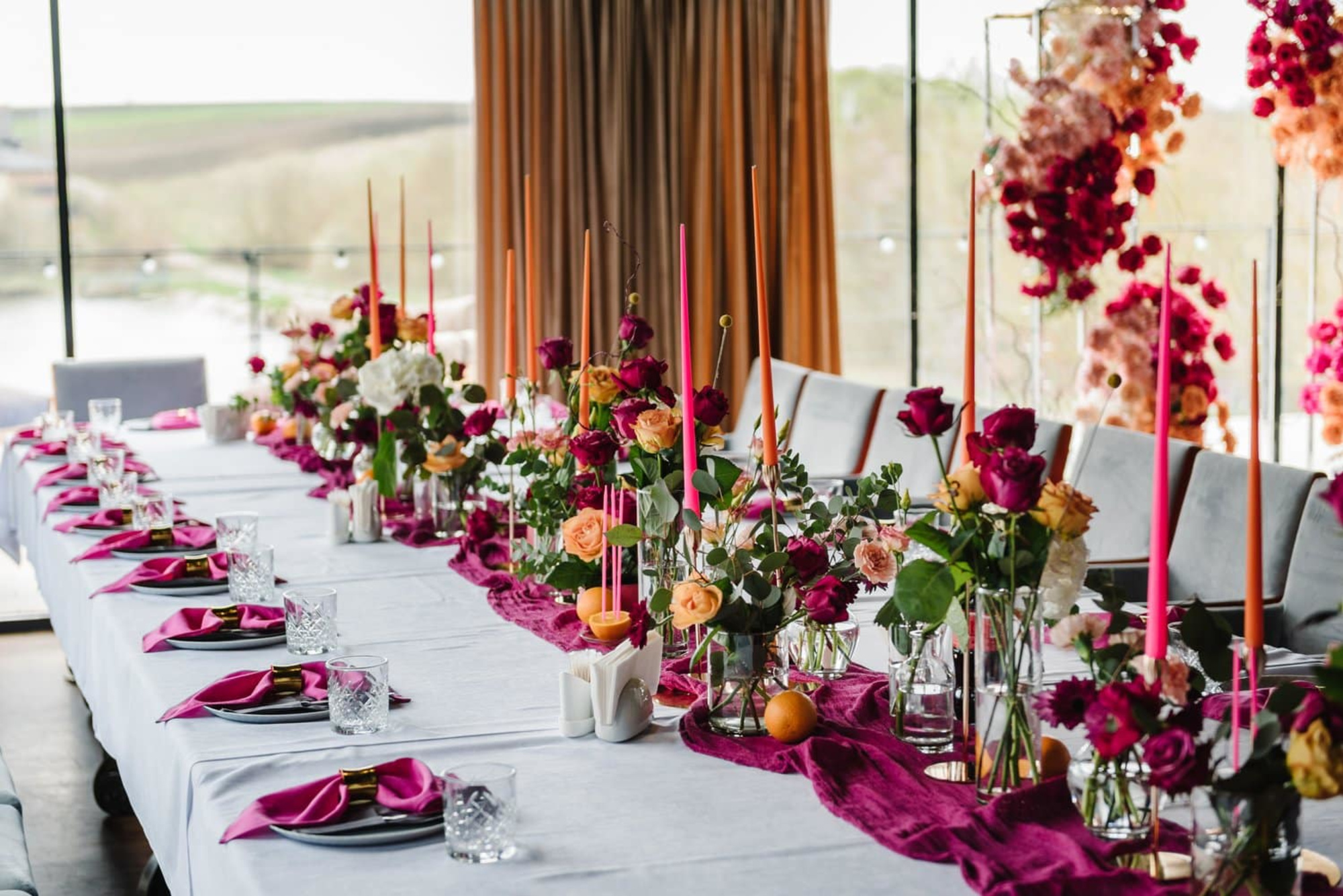 Colorful wedding reception table with vibrant floral centerpieces and tall taper candles along a long white-draped banquet table.