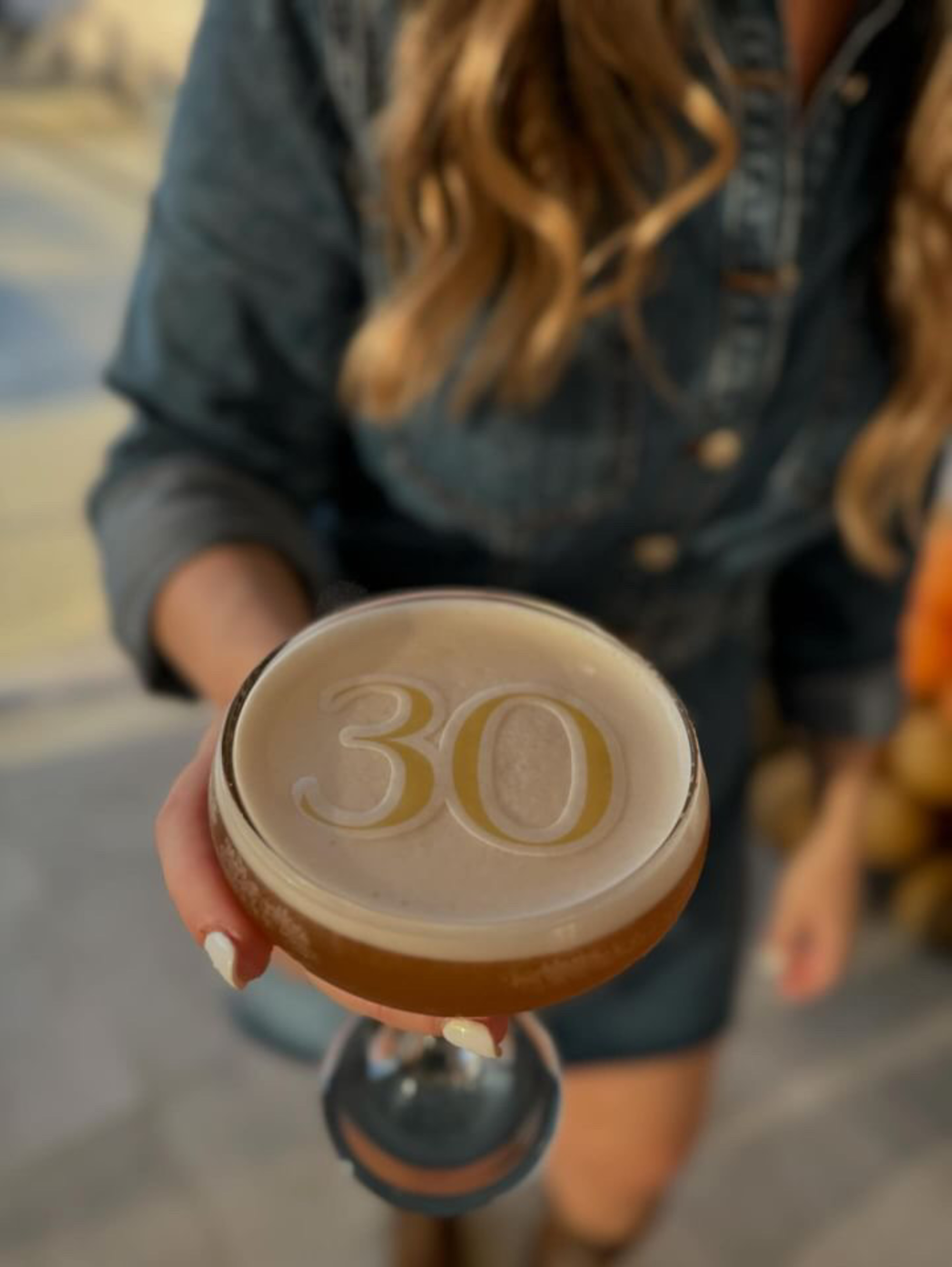 Person holding a cocktail with the number 30 printed in foam, captured in a close-up view.