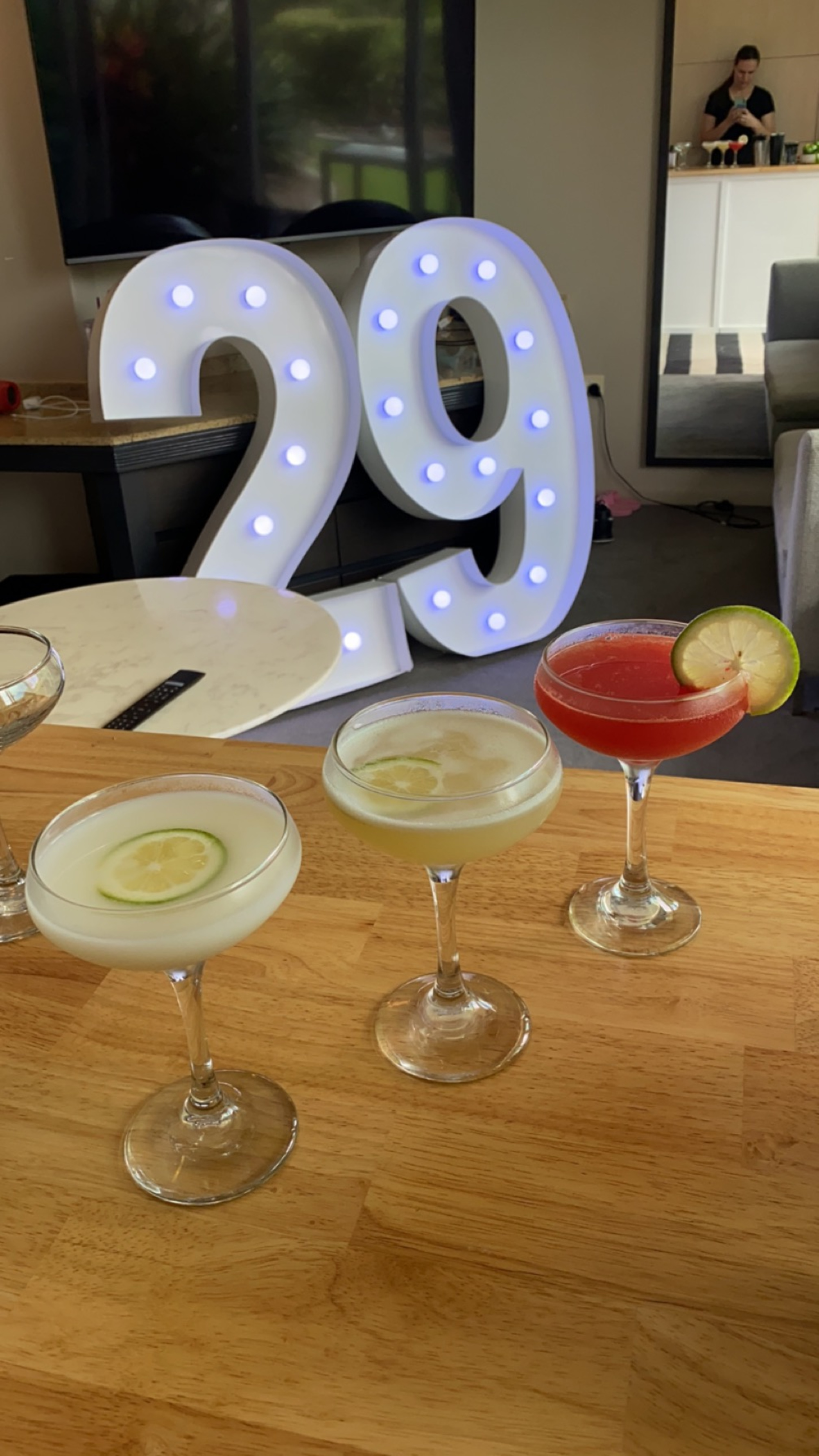 Colorful cocktails on a wooden bar in front of large illuminated 29 marquee numbers.