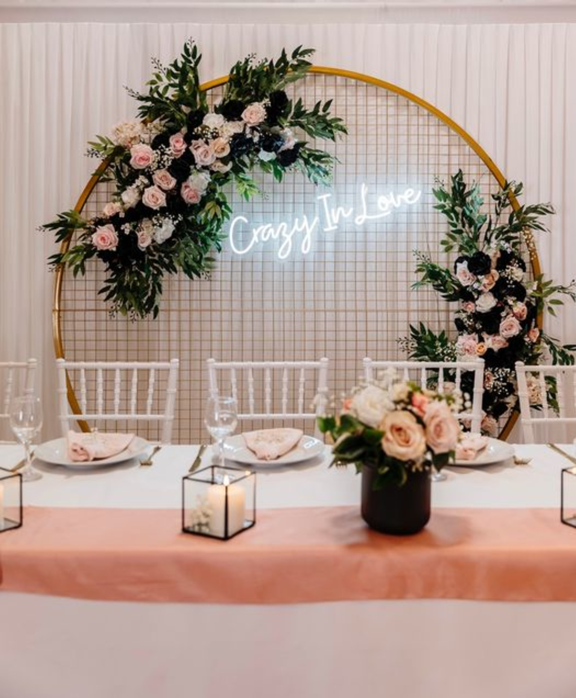Romantic wedding reception table with pink florals and a circular neon sign reading Crazy In Love.