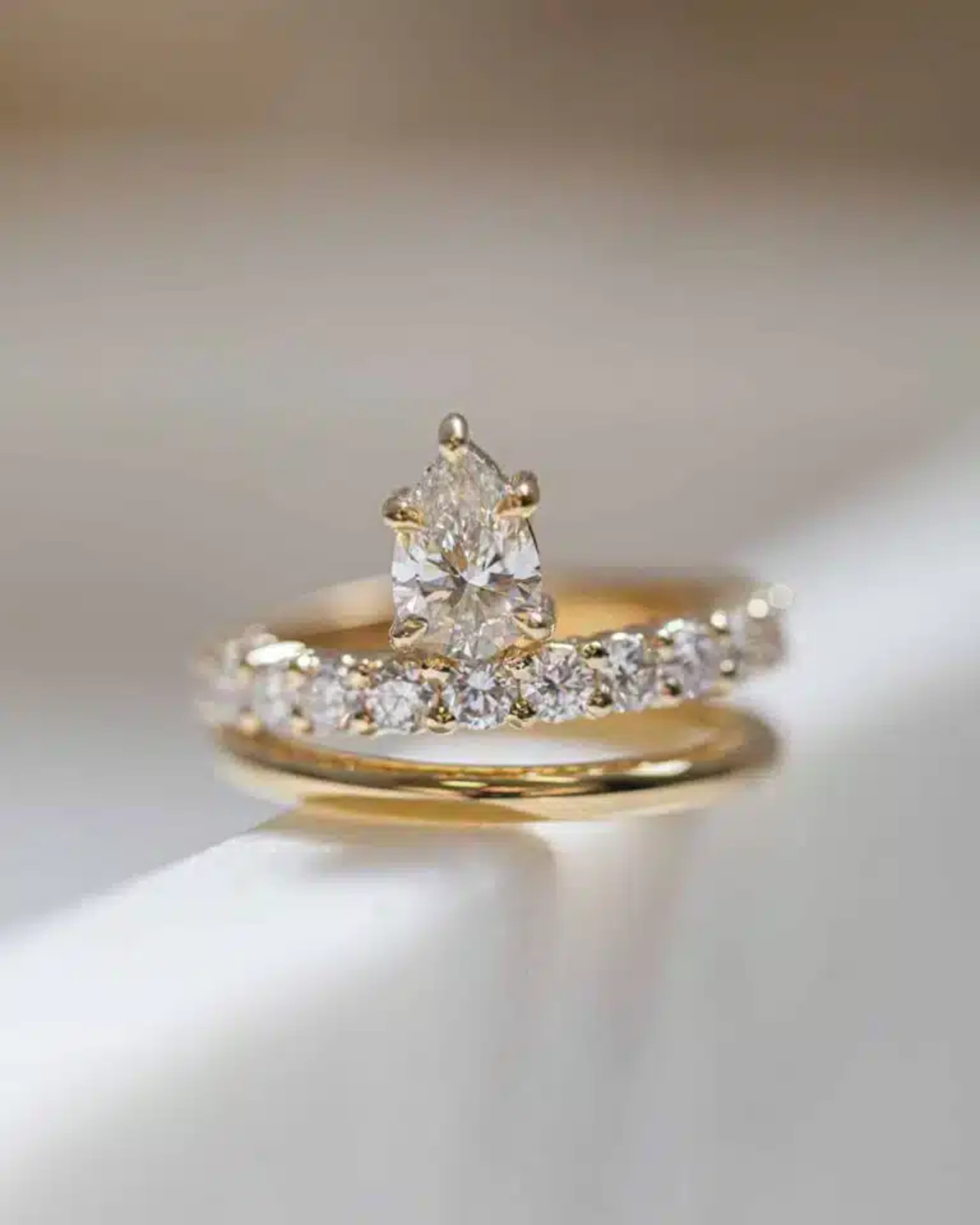 Close-up of a gold diamond engagement ring stacked with a matching diamond wedding band on a light surface.