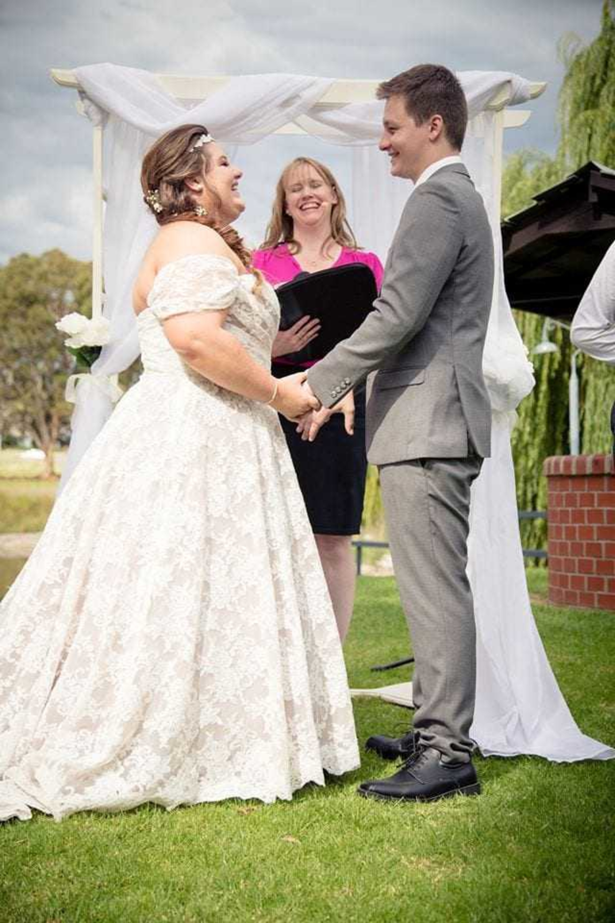 Bride and groom hold hands during an outdoor wedding ceremony under a white arch.