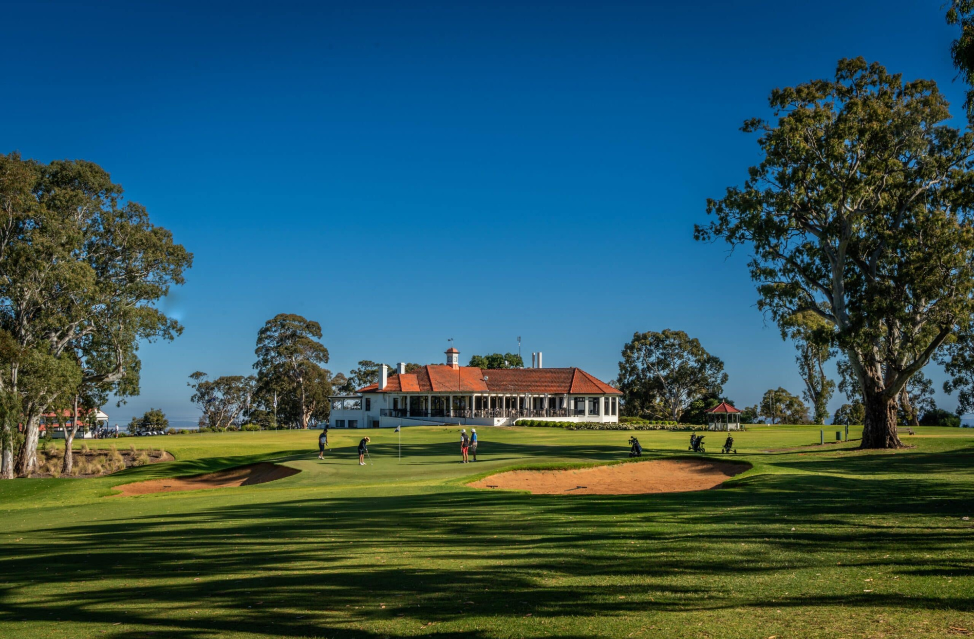 Elegant country club building overlooking a manicured golf course under a clear blue sky.