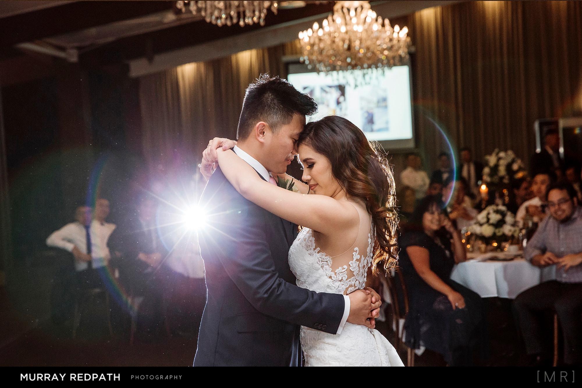 Bride and groom share a romantic first dance under chandeliers at their indoor wedding reception.