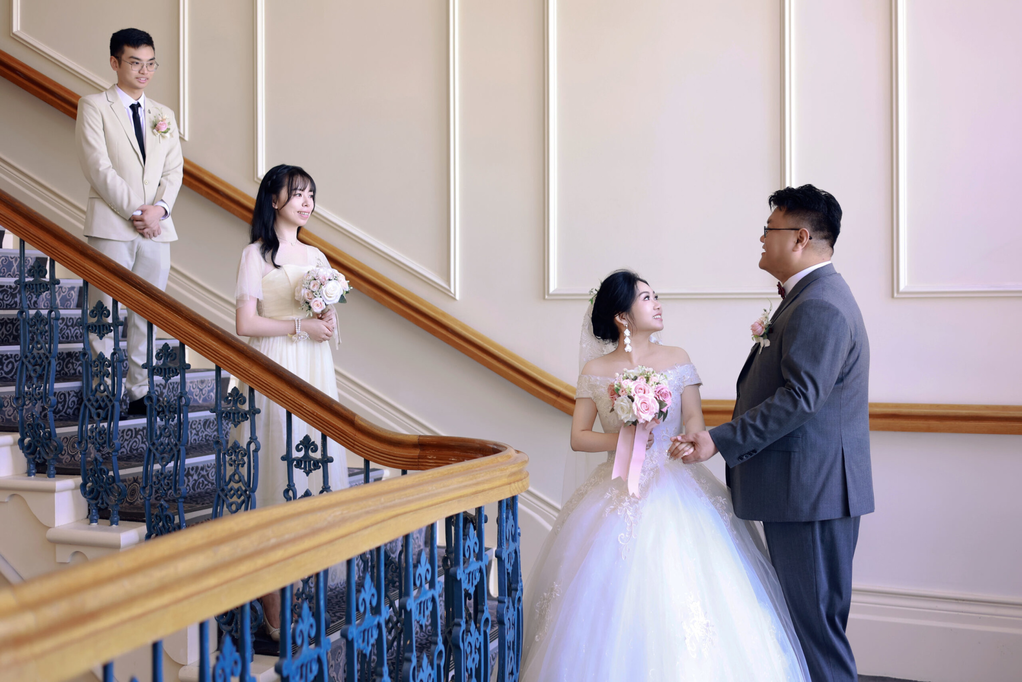 Bride and groom pose on an elegant staircase with their wedding party holding pastel bouquets.