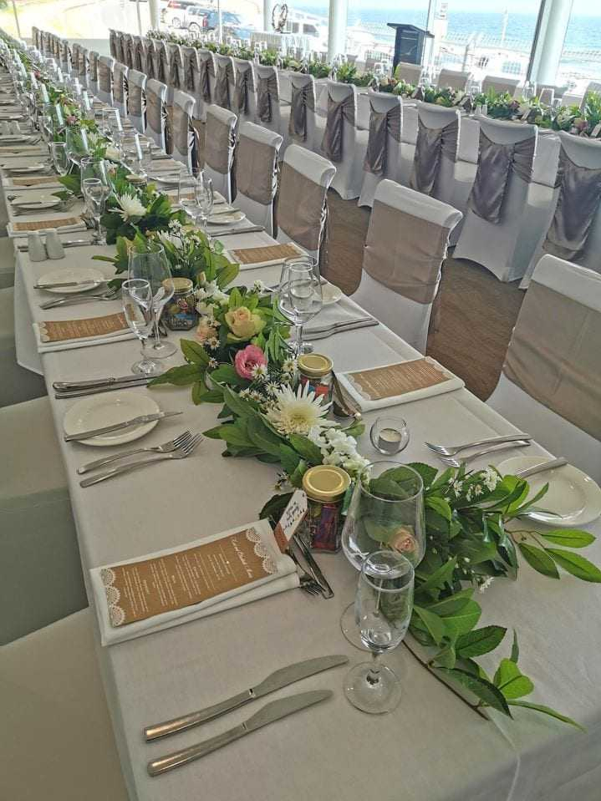 Elegant beachside wedding reception with long banquet tables, white linens, and greenery garland centerpieces.