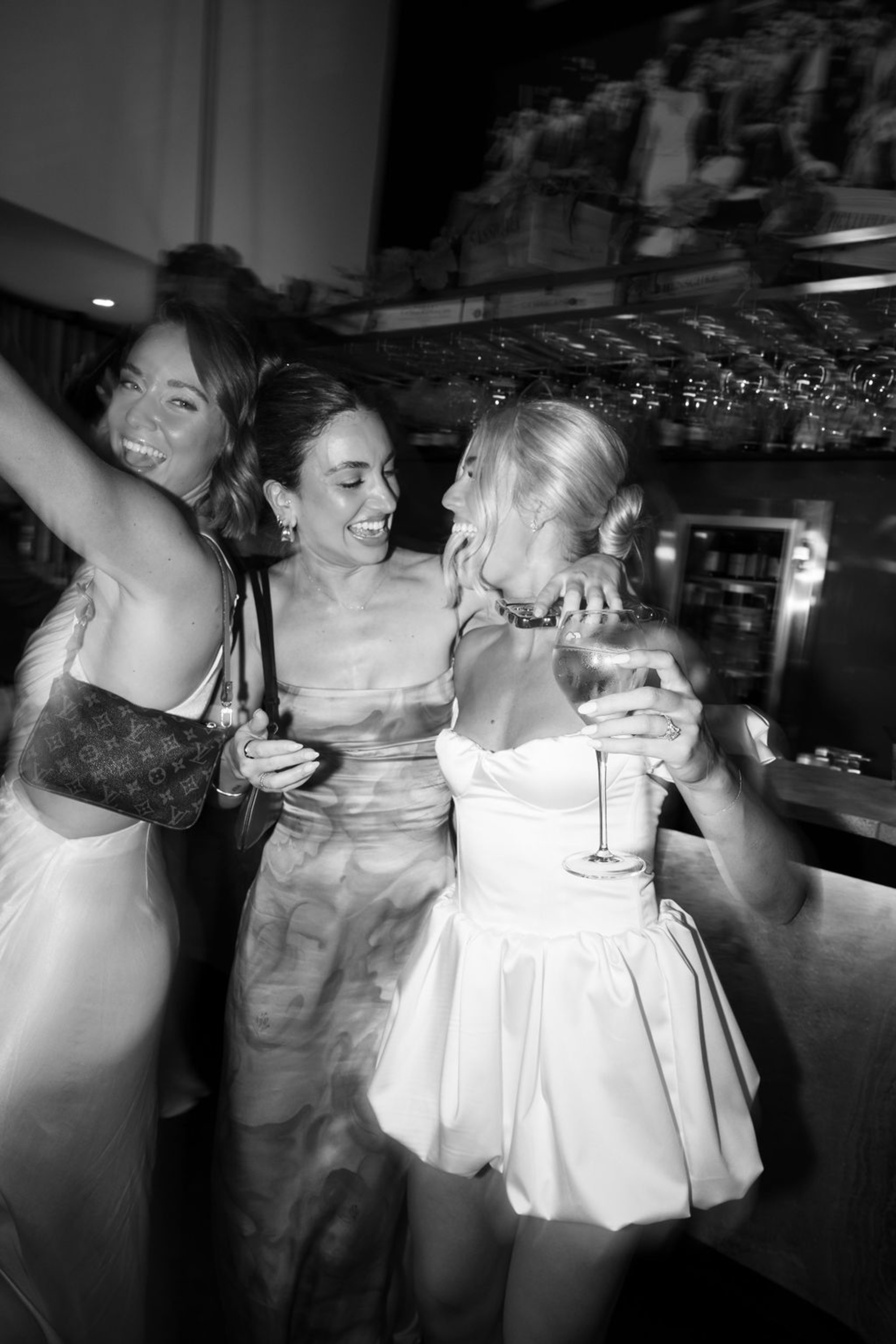 Candid black and white photo of the bride celebrating with friends and drinks at the wedding reception bar.