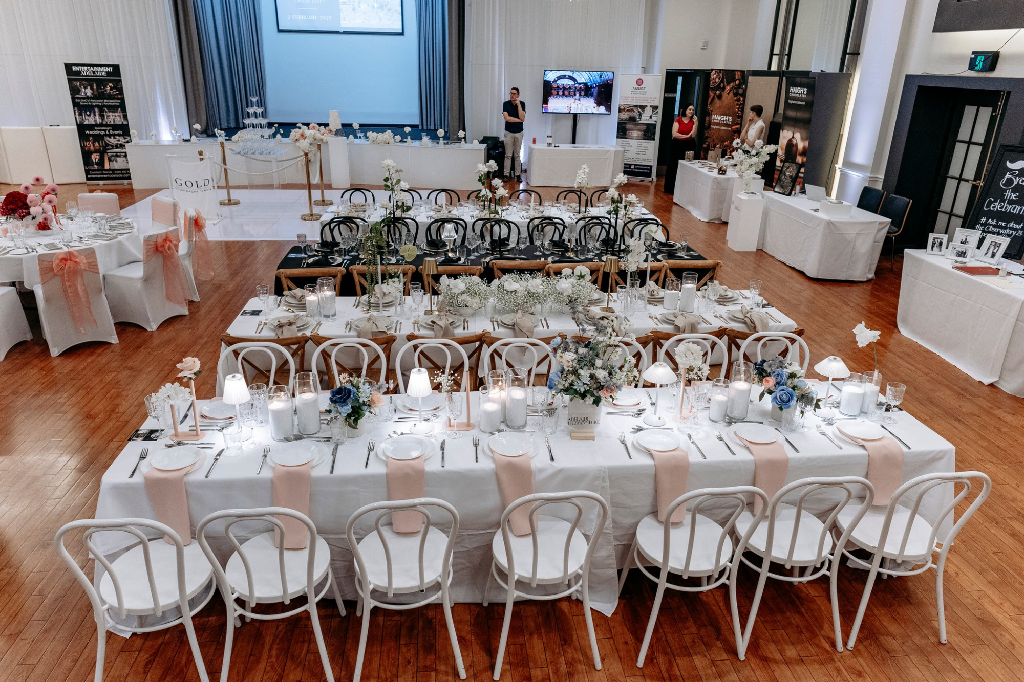 Elegant indoor wedding reception setup with long banquet tables, floral centerpieces, and candlelit decor.