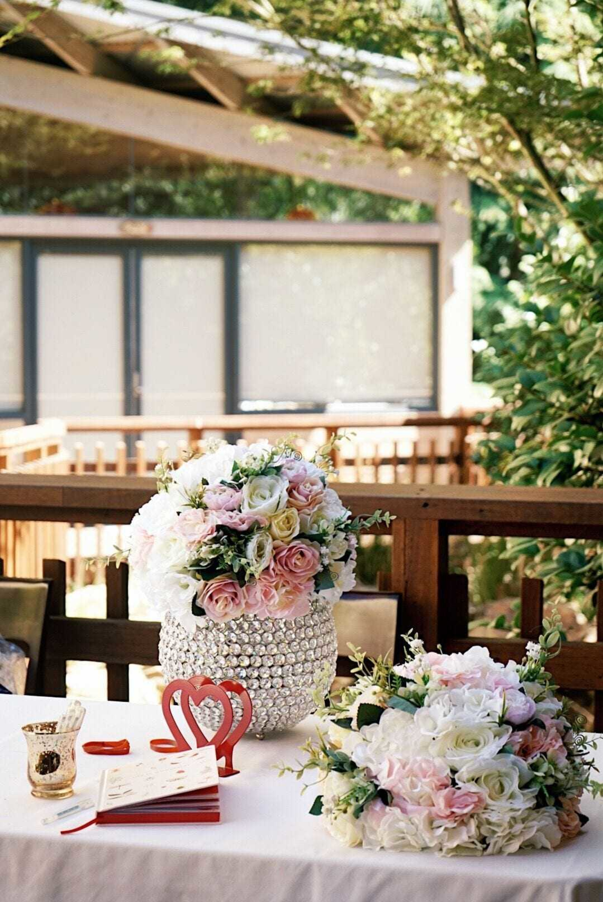 Outdoor wedding guest book table with pastel rose arrangements in a crystal vase and a red heart detail.