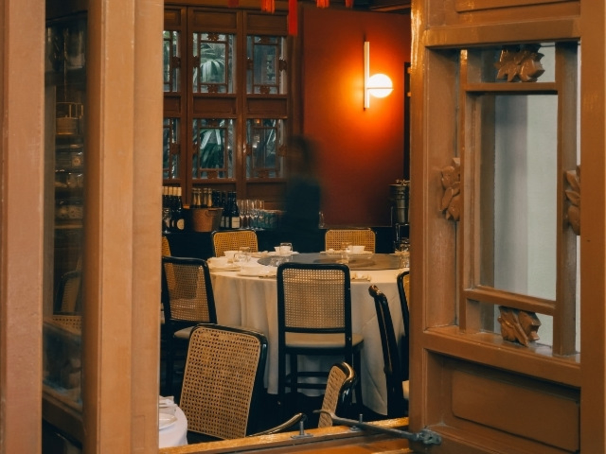 Cozy indoor restaurant-style wedding reception with round tables and warm ambient lighting viewed through an open window.