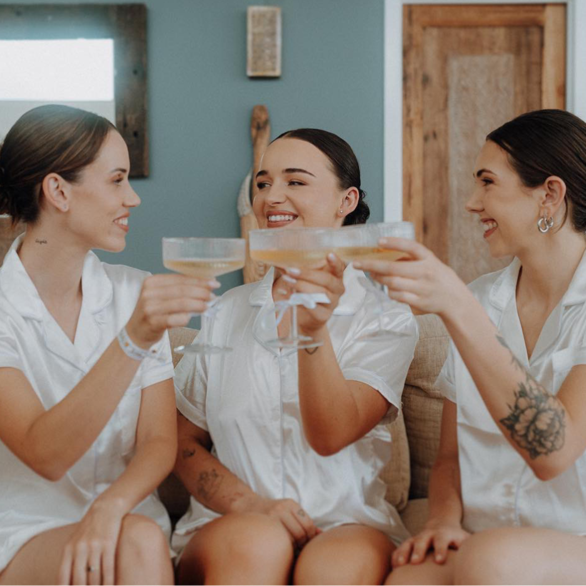 Three bridesmaids in matching satin pajamas share a champagne toast while getting ready.