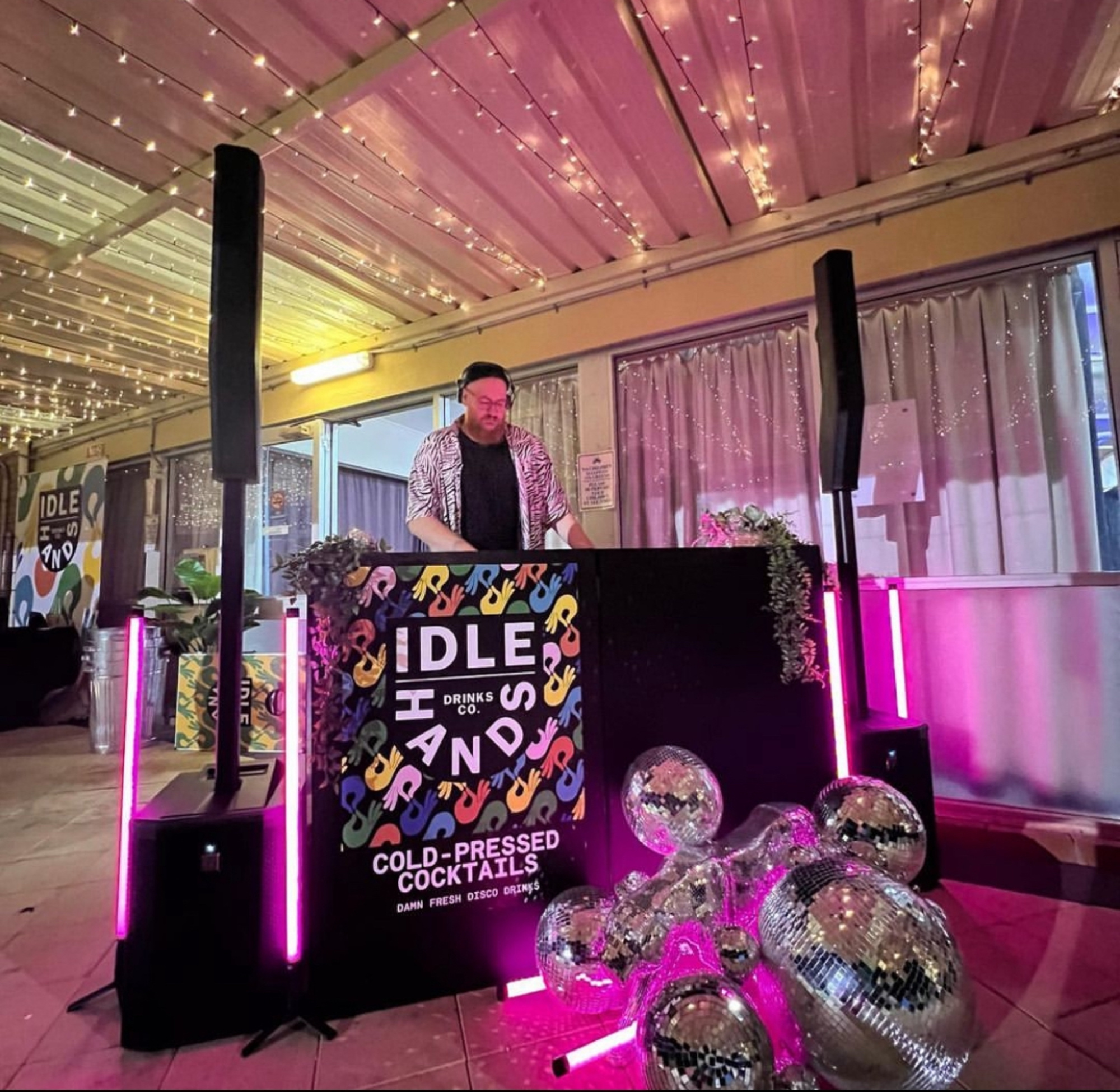 DJ performing at a wedding reception with disco balls, neon lights, and a colorful Idle Hands drinks bar.