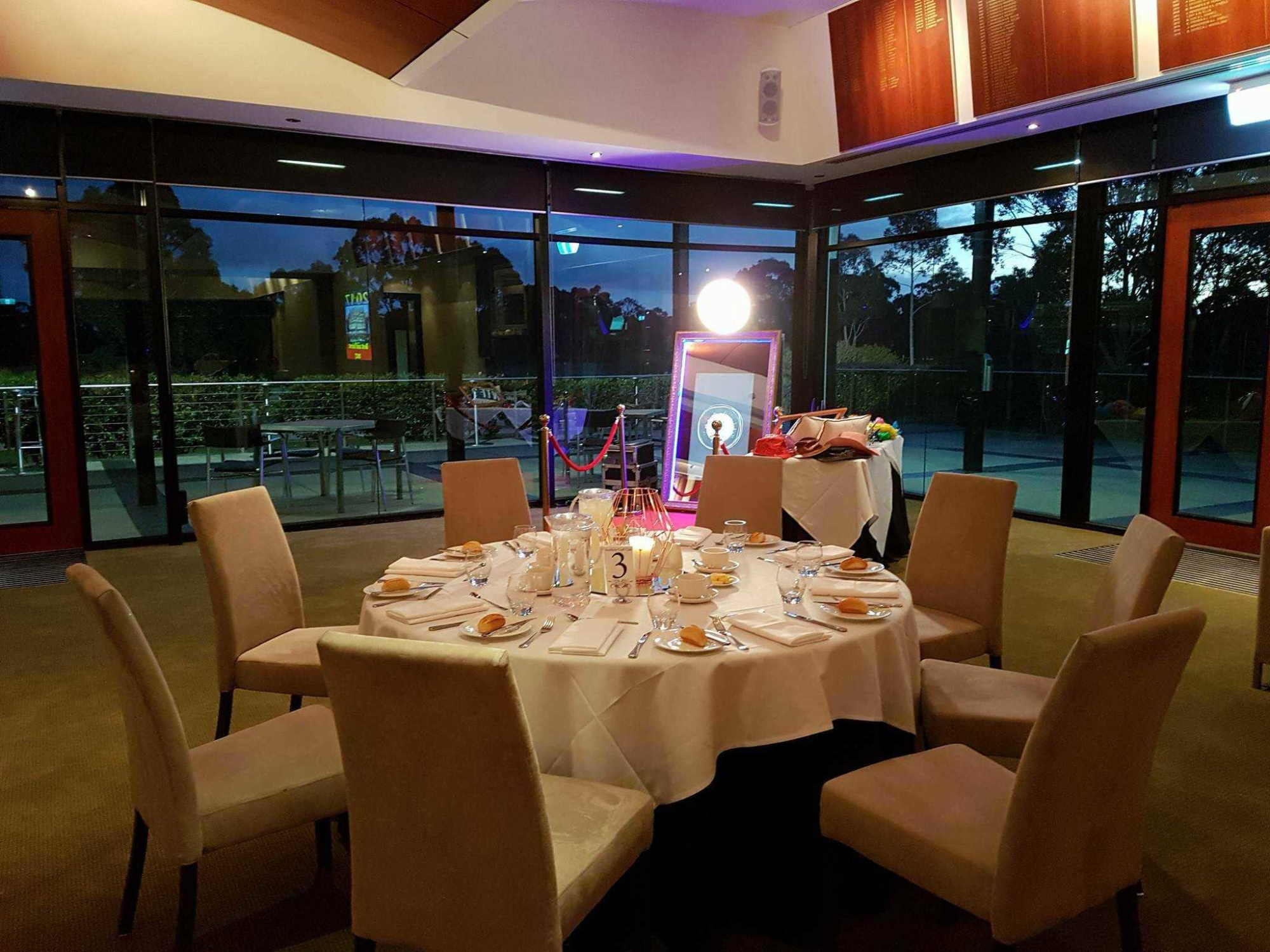 Elegant evening wedding reception table set for guests in a modern glass-walled venue.