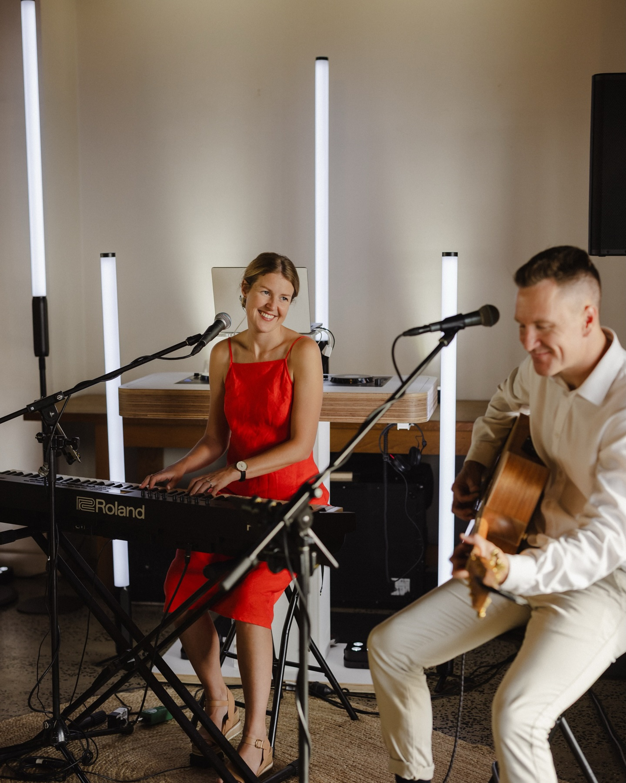 Smiling acoustic duo performing with keyboard and guitar in a modern indoor wedding setting.