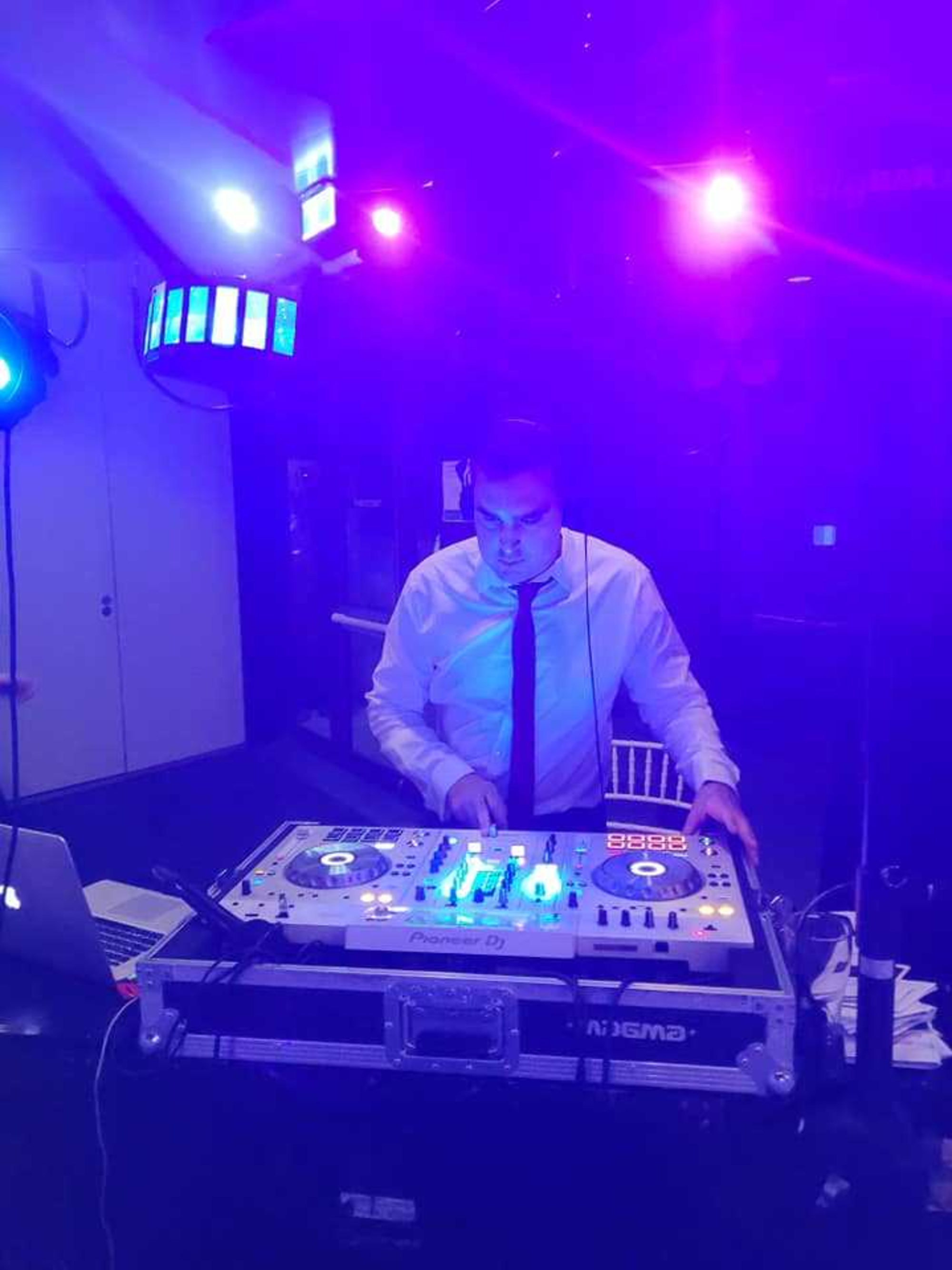 Wedding DJ mixing music at a glowing DJ booth under vibrant purple reception lights.