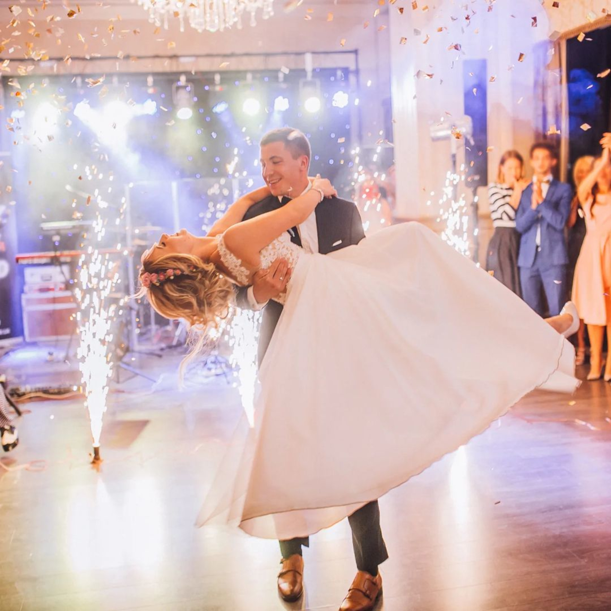 Groom lifts bride on the dance floor surrounded by indoor fireworks and cheering guests.
