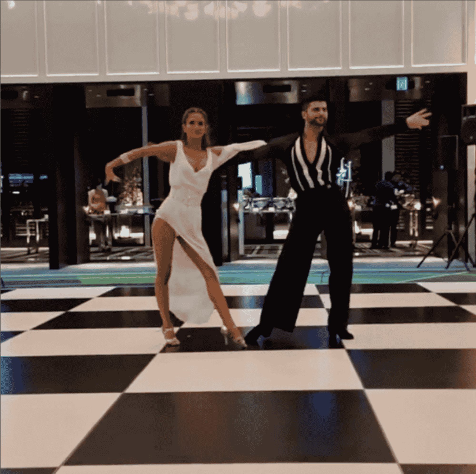 Couple performing a dramatic ballroom dance on a black and white checkered wedding reception floor.