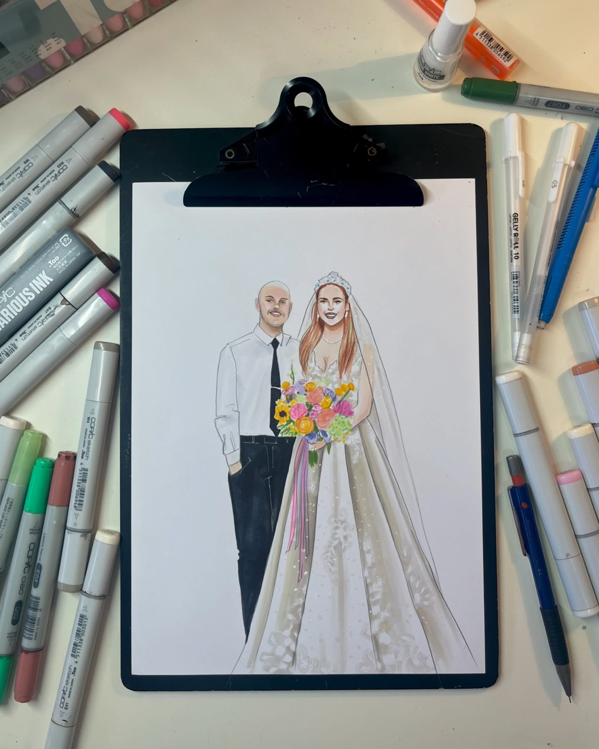 Illustrated wedding couple portrait on a clipboard surrounded by markers and art supplies.