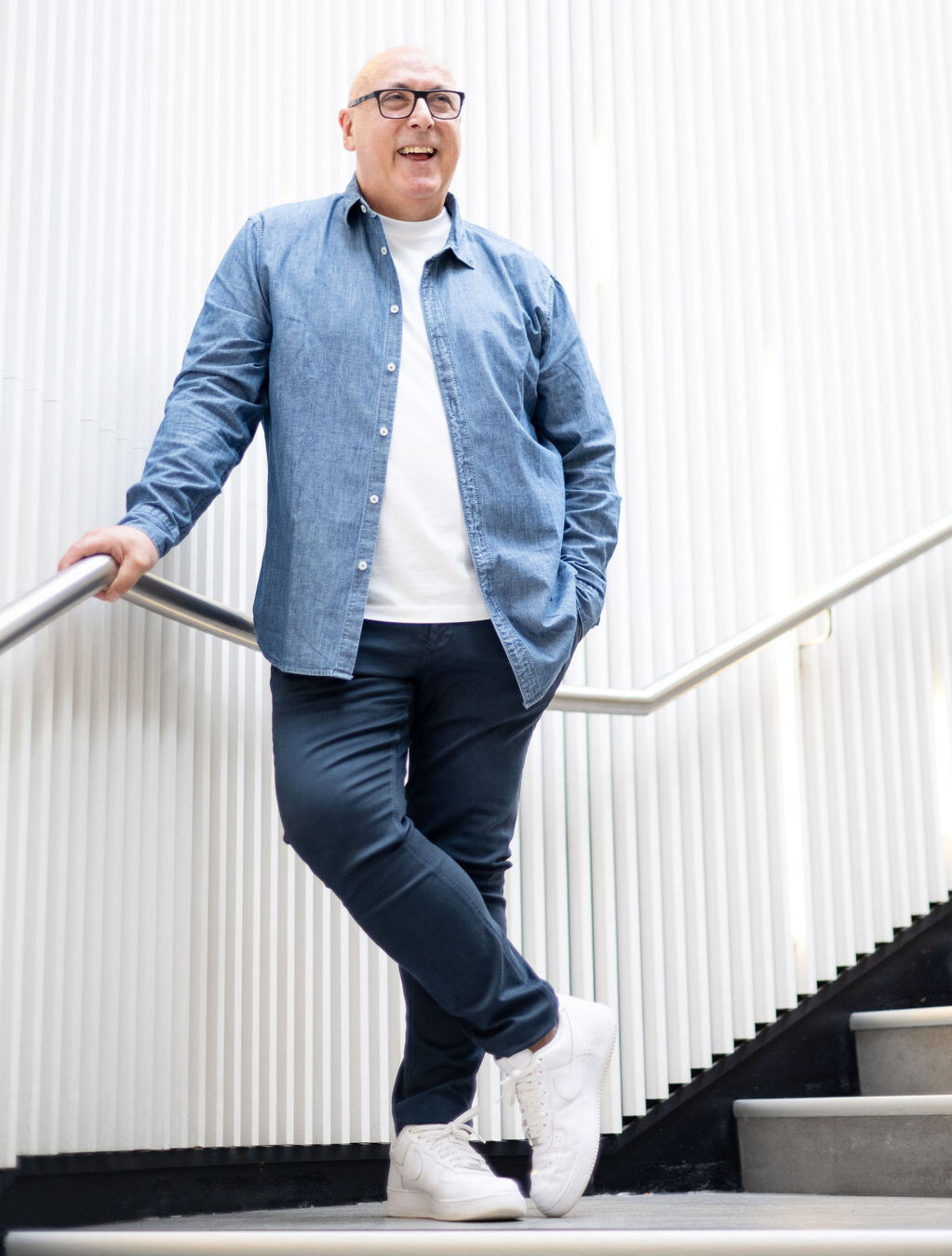 Smiling wedding vendor poses casually on a modern staircase with white textured walls.