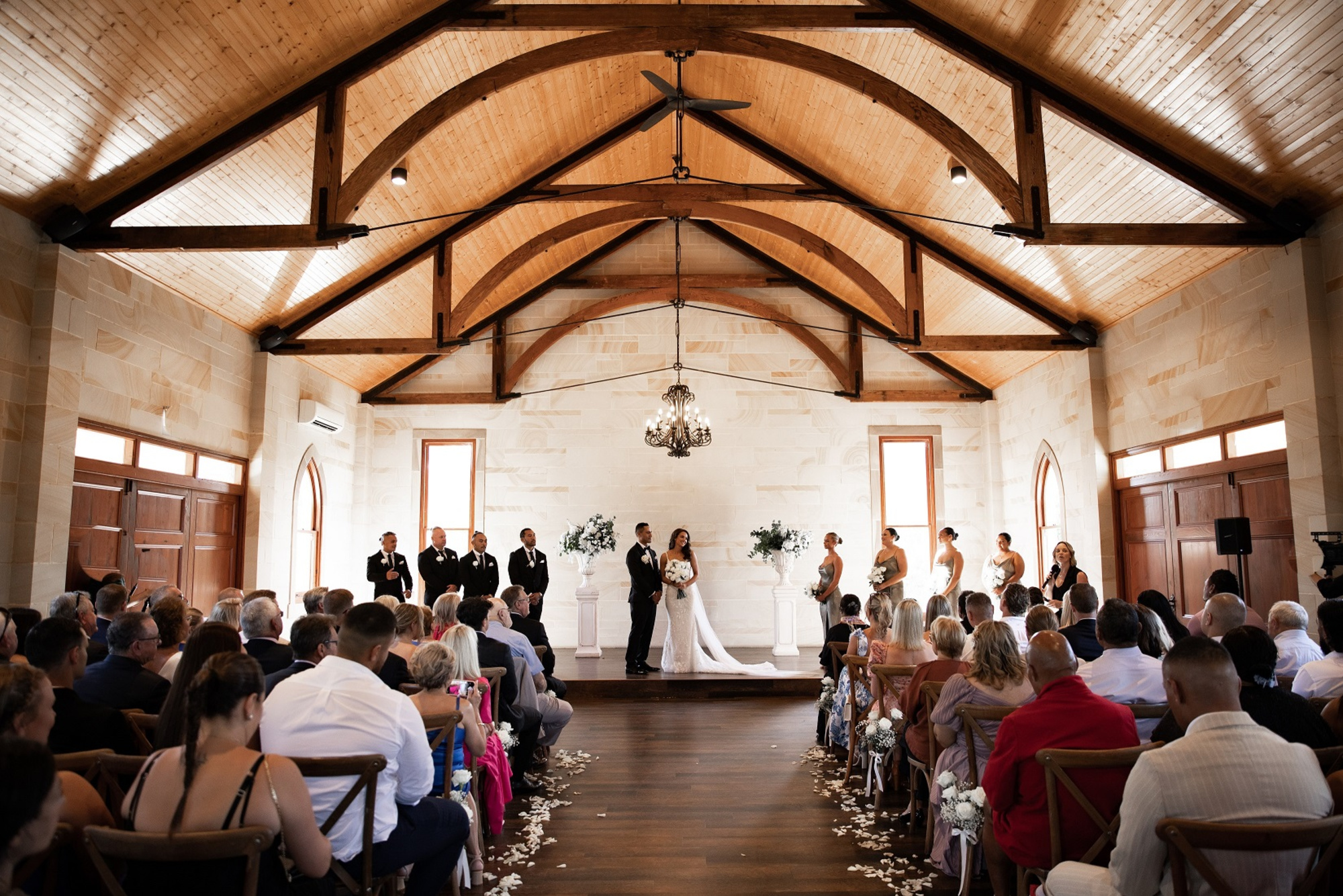 Indoor wedding ceremony in a rustic chapel with wooden beams, seated guests, and the couple standing at the altar.