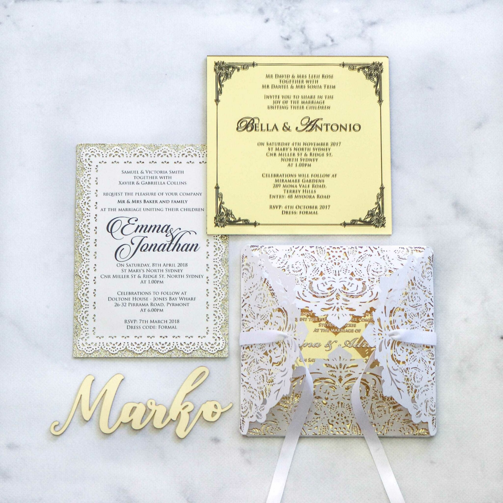 Elegant gold and white wedding invitations with a laser cut pocket and wooden name place card on a marble surface.