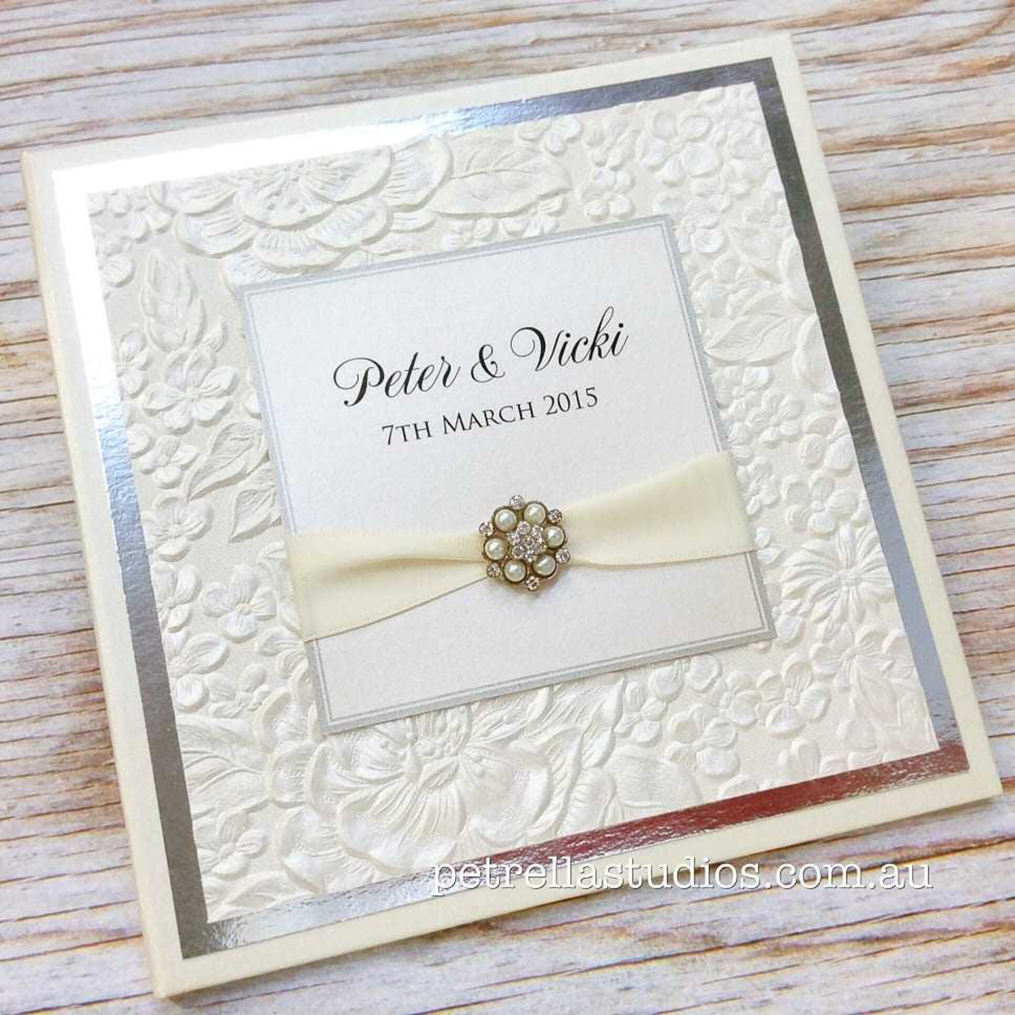 Elegant embossed floral wedding invitation with ivory ribbon and pearl brooch for Peter and Vicki.