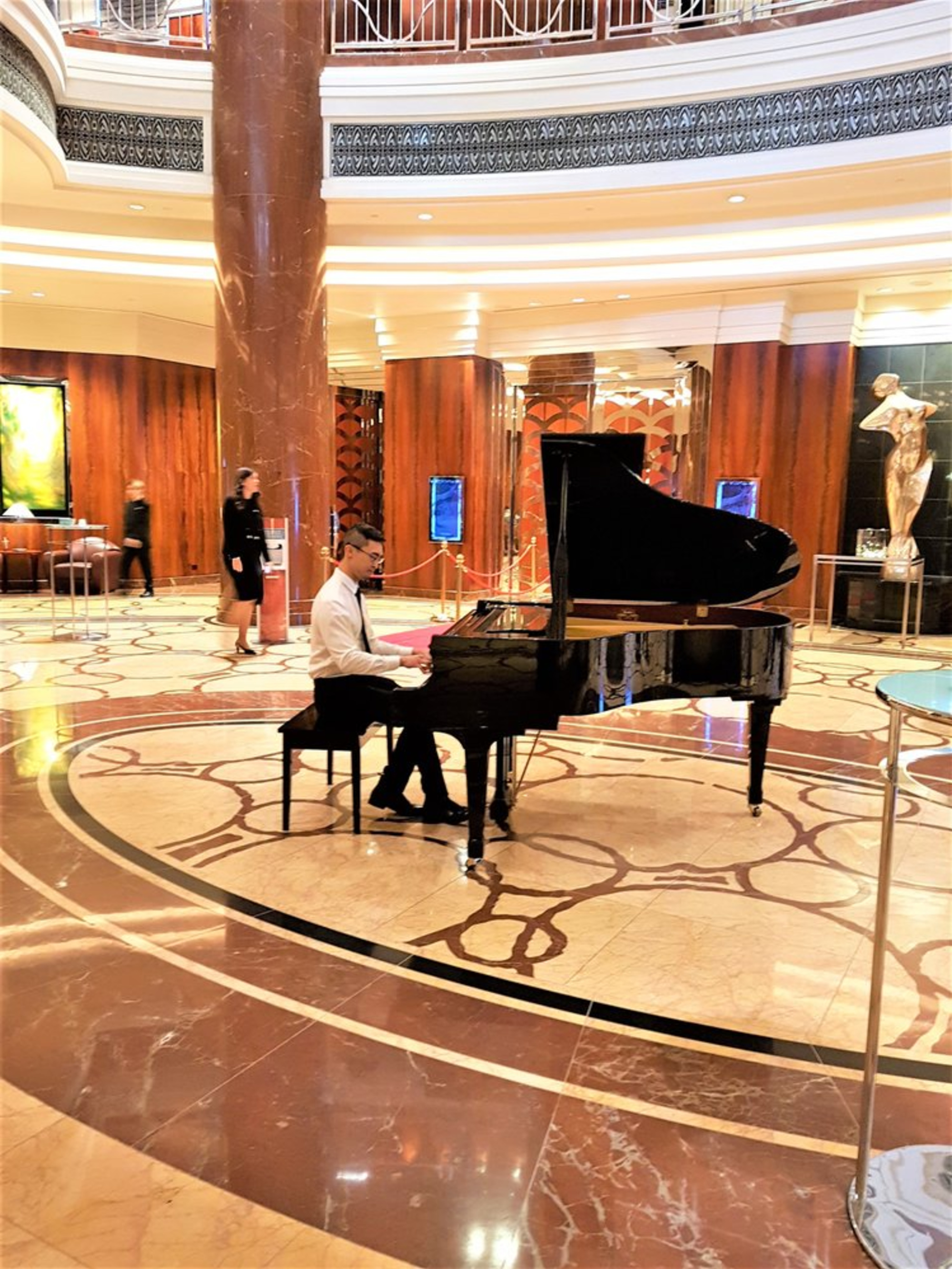 Pianist performing on a grand piano in an elegant hotel lobby with marble floors and warm lighting.