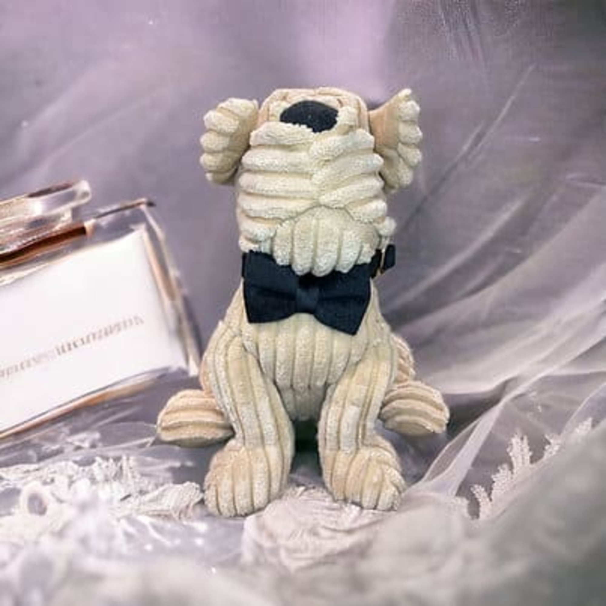 Corduroy-style stuffed dog with a black bow tie displayed as whimsical wedding decor on soft fabric.