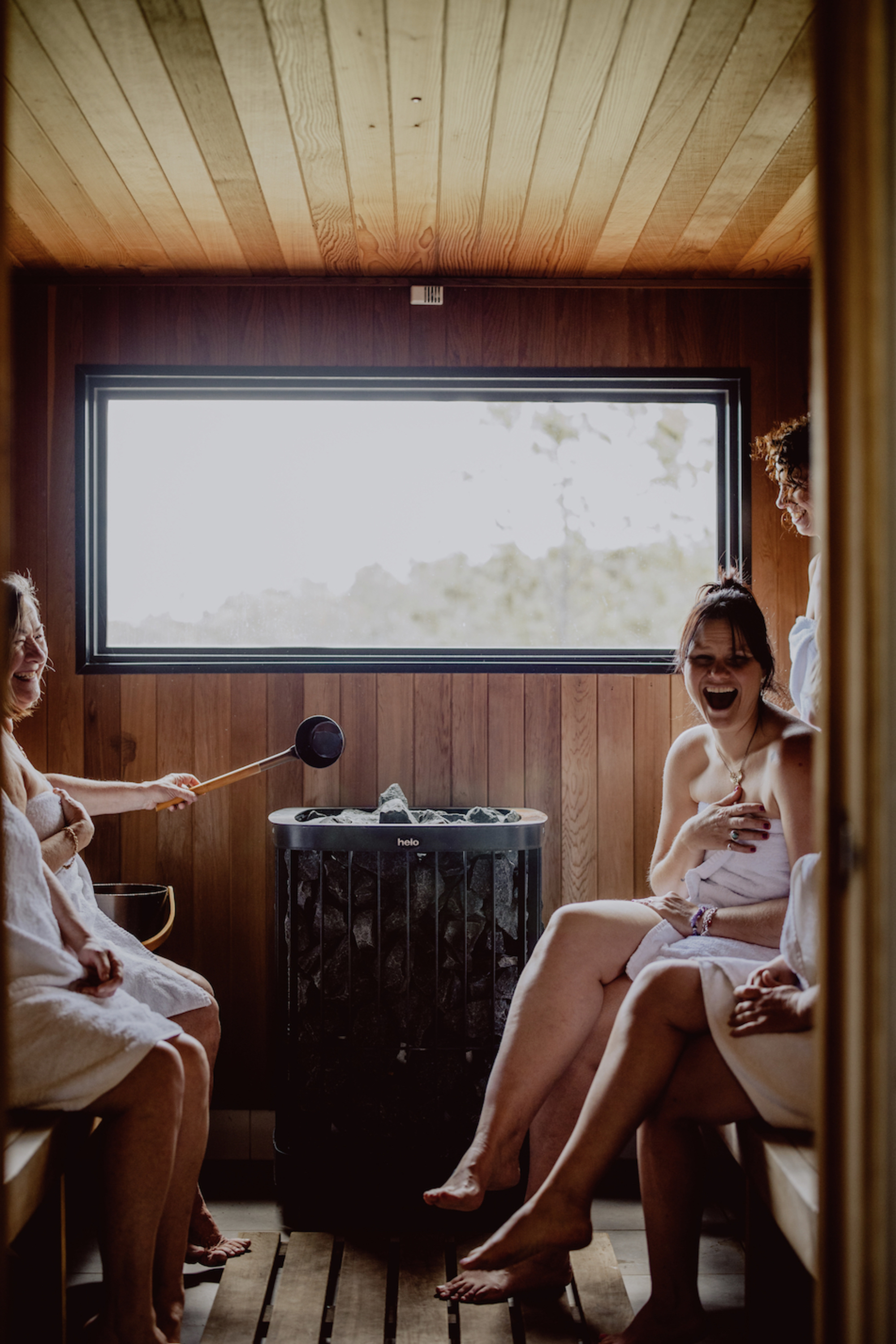 Bridal party in towels laughing and relaxing together in a wooden sauna room.