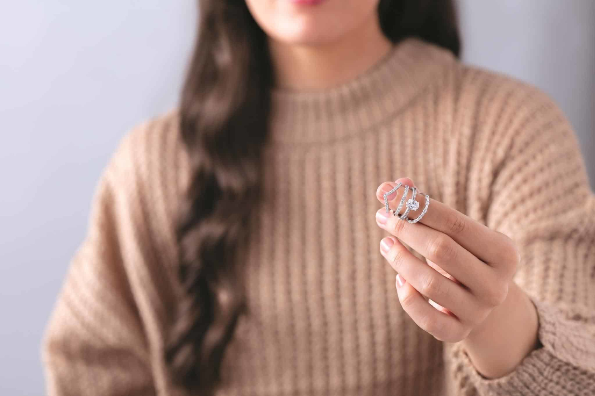 Person in a knit sweater holding a stack of sparkling silver diamond rings close to the camera.