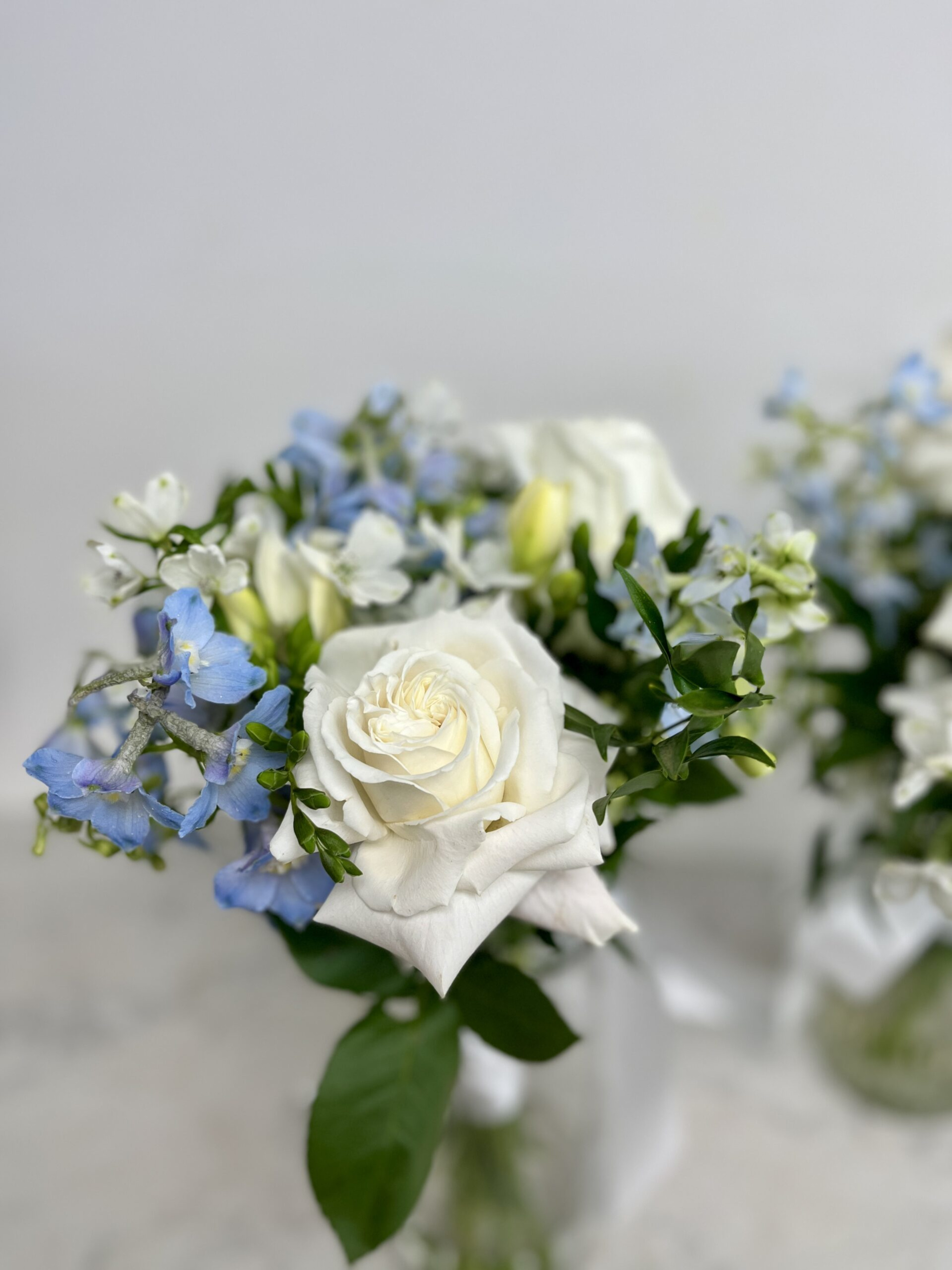 Close-up of a white and blue wedding bouquet with roses and greenery in a glass vase.