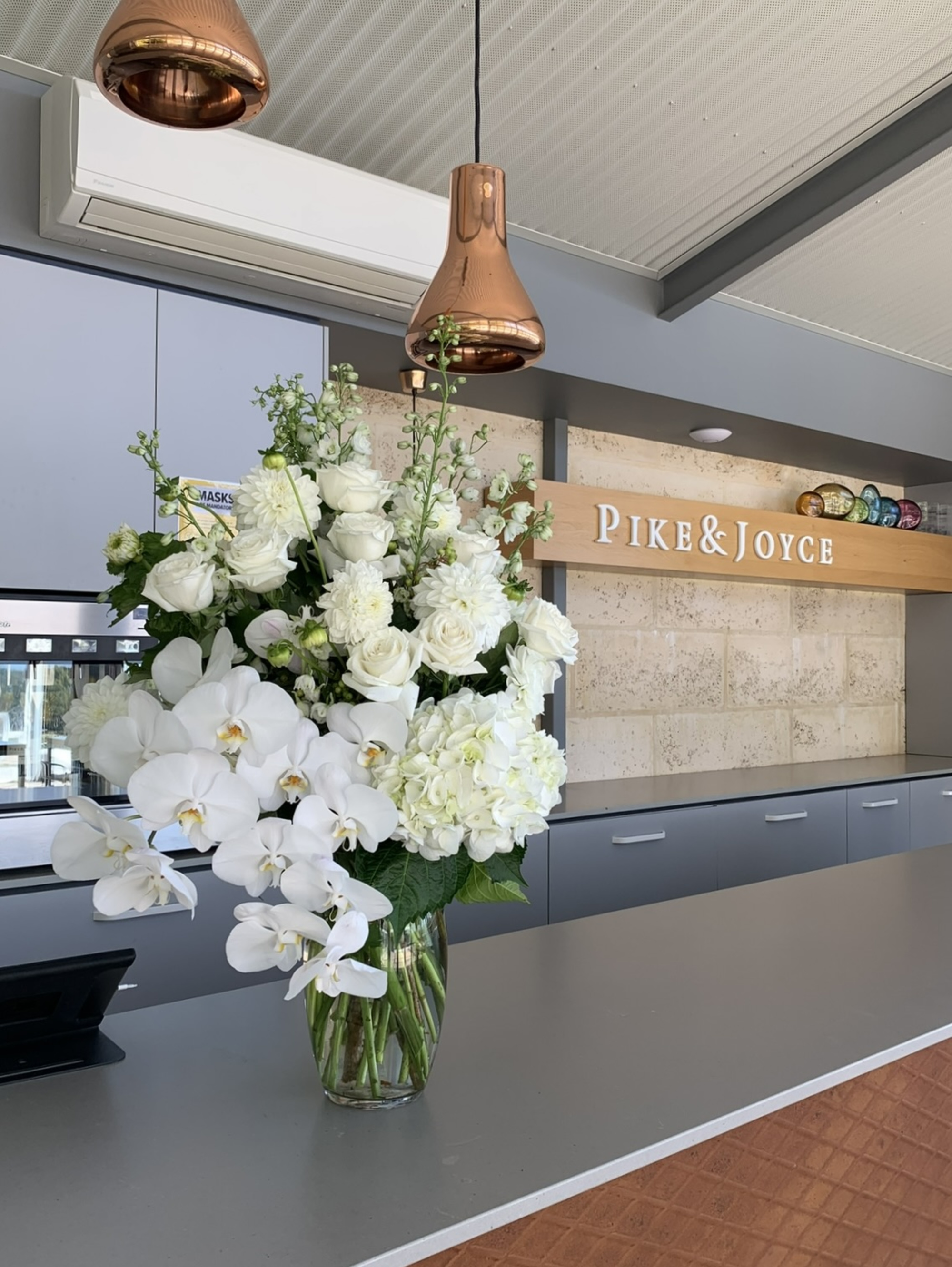 Large white floral centerpiece with orchids and roses on a modern counter at Pike & Joyce venue.