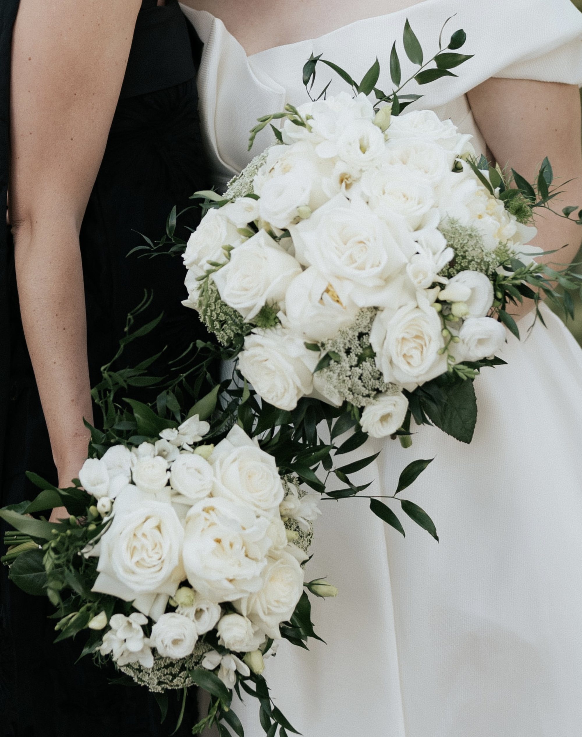 Close-up of two elegant white rose bridal bouquets with lush greenery held by members of the wedding party.
