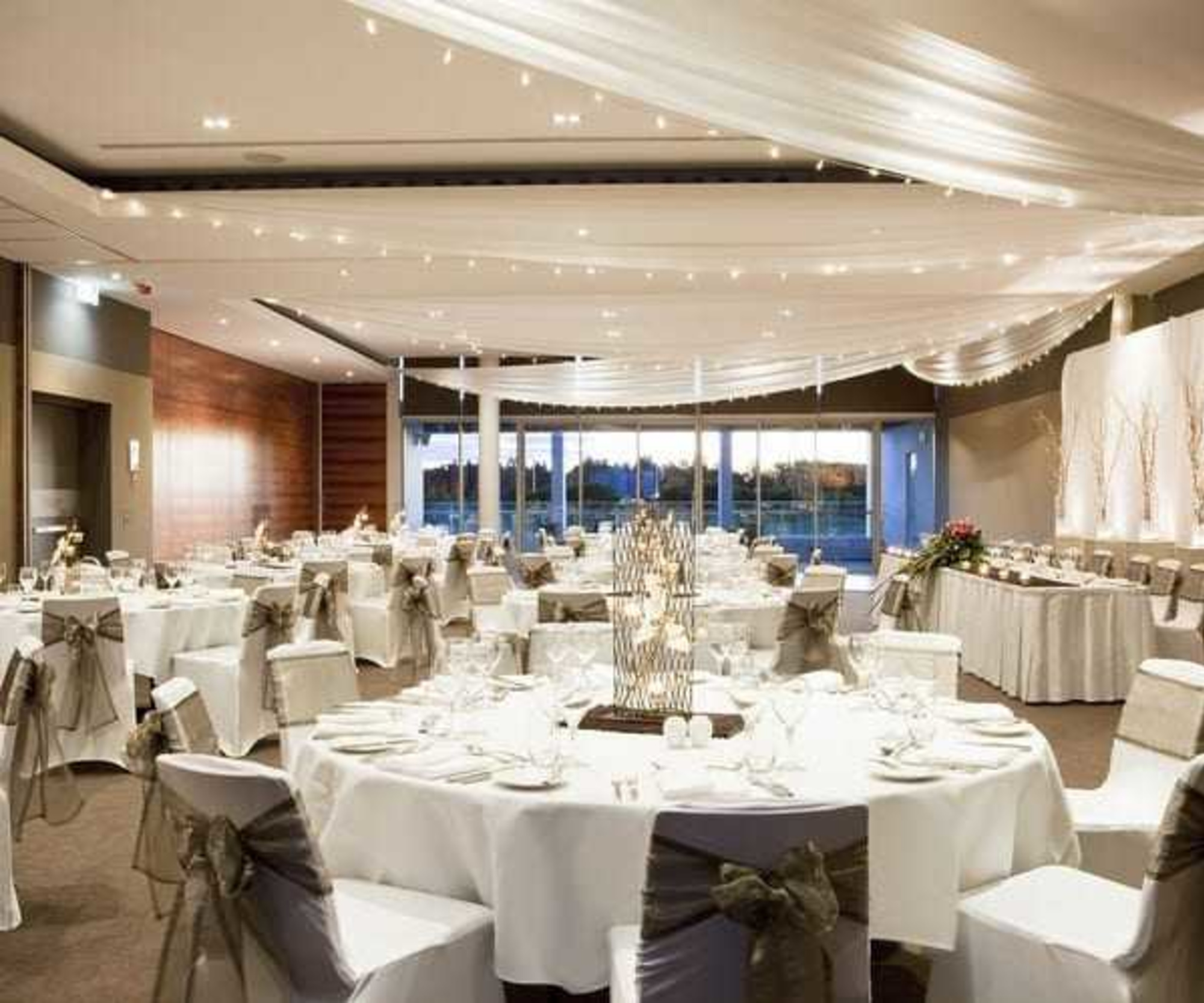 Elegant indoor wedding reception venue with draped ceiling, fairy lights, and round tables set for dinner.