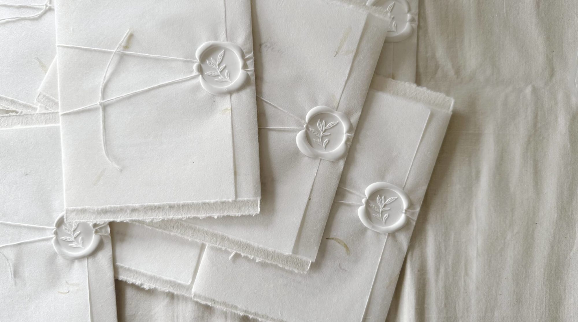 Handmade white wedding invitations tied with string and sealed with white wax stamps featuring a botanical motif.