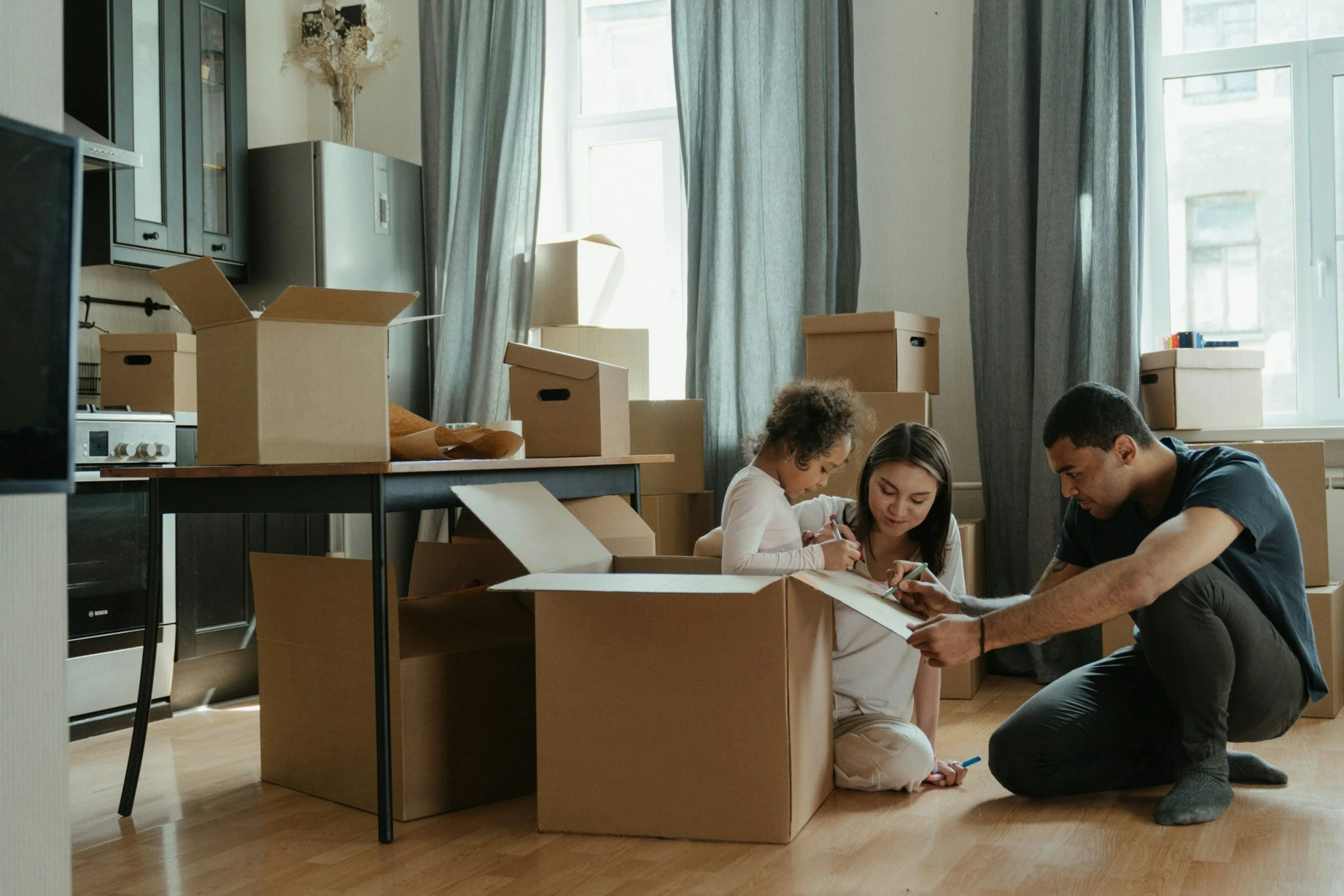 Family sitting on the floor among moving boxes, drawing together in their new home.