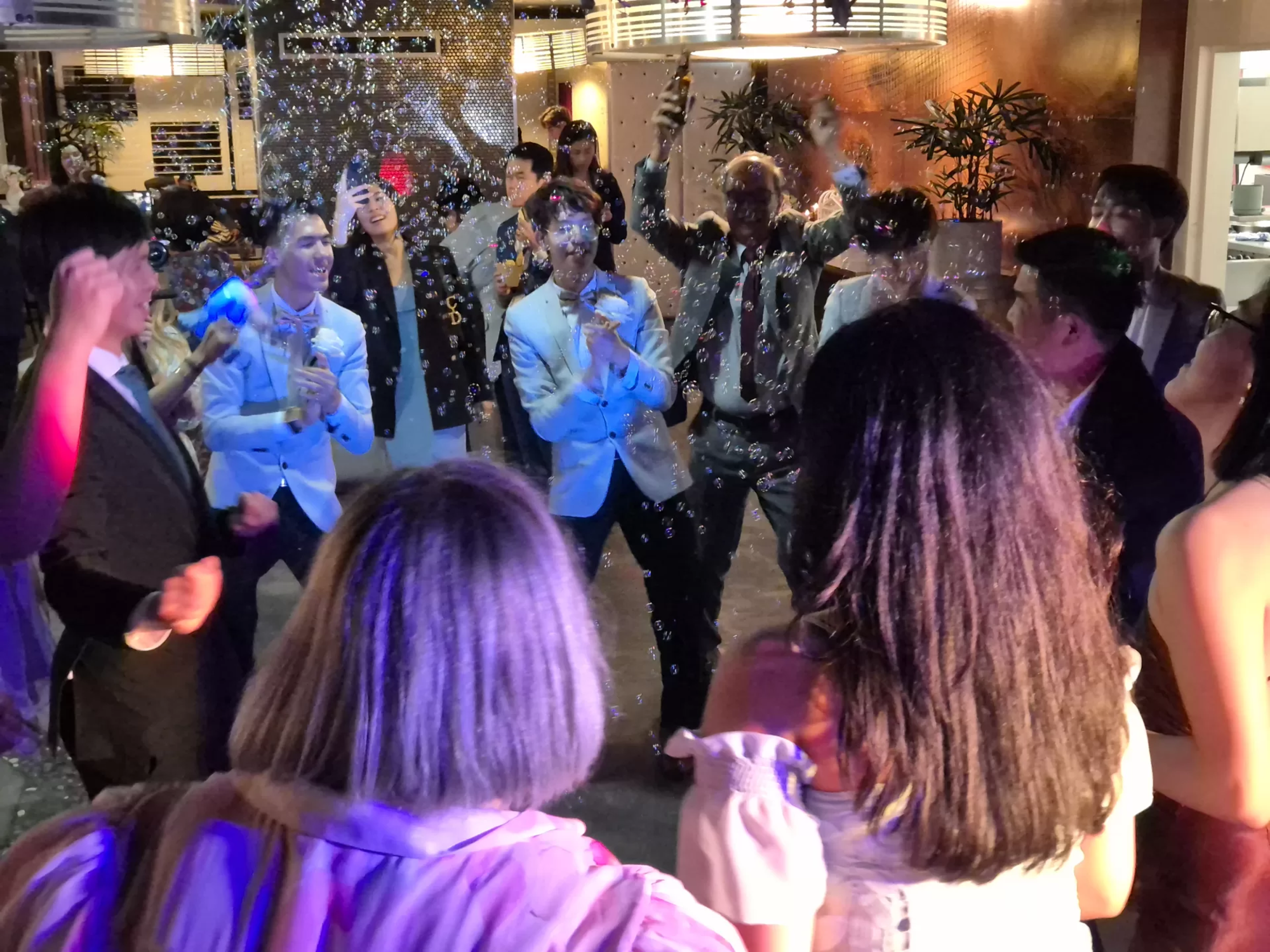 Guests dance on an indoor wedding dance floor surrounded by bubbles and colorful lights.