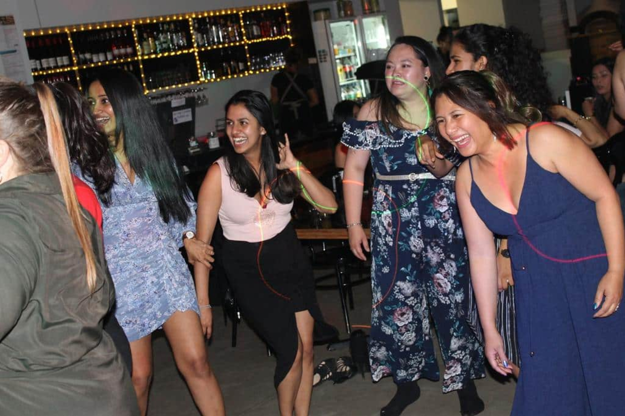 Group of guests laughing and dancing together on a lively indoor wedding reception dance floor.