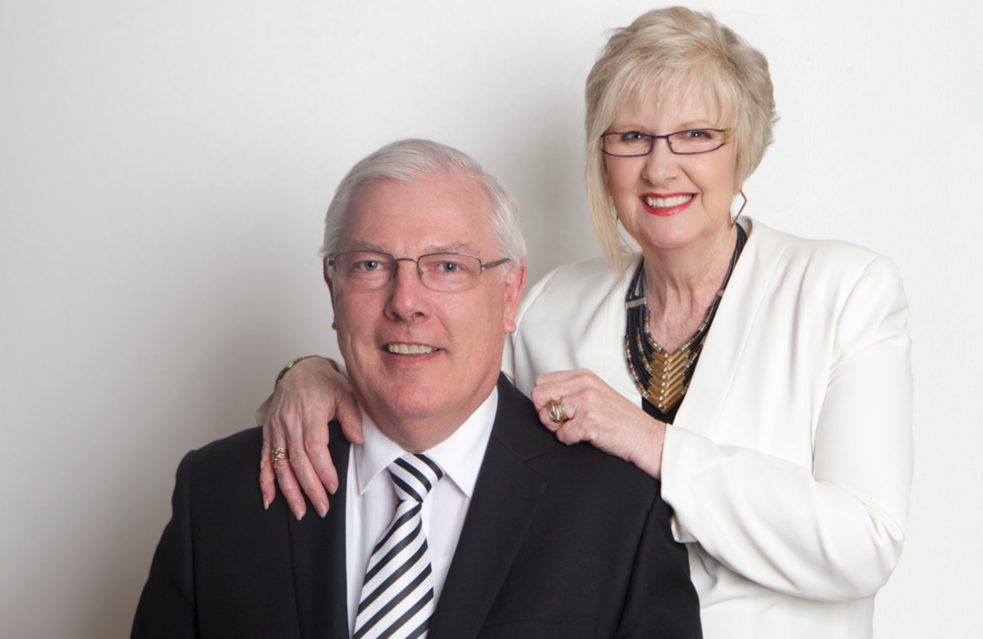 Professional studio portrait of a smiling mature couple in formal black and white attire against a plain background.