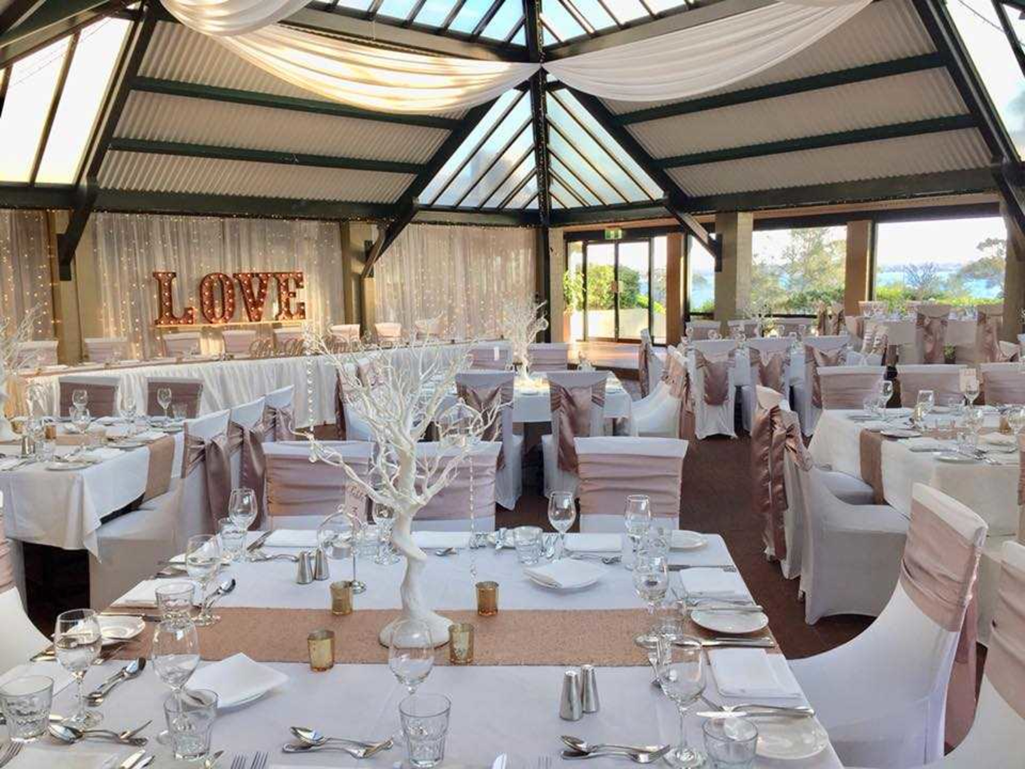 Elegant indoor wedding reception setup with blush and white decor, draped ceiling, and illuminated LOVE sign.