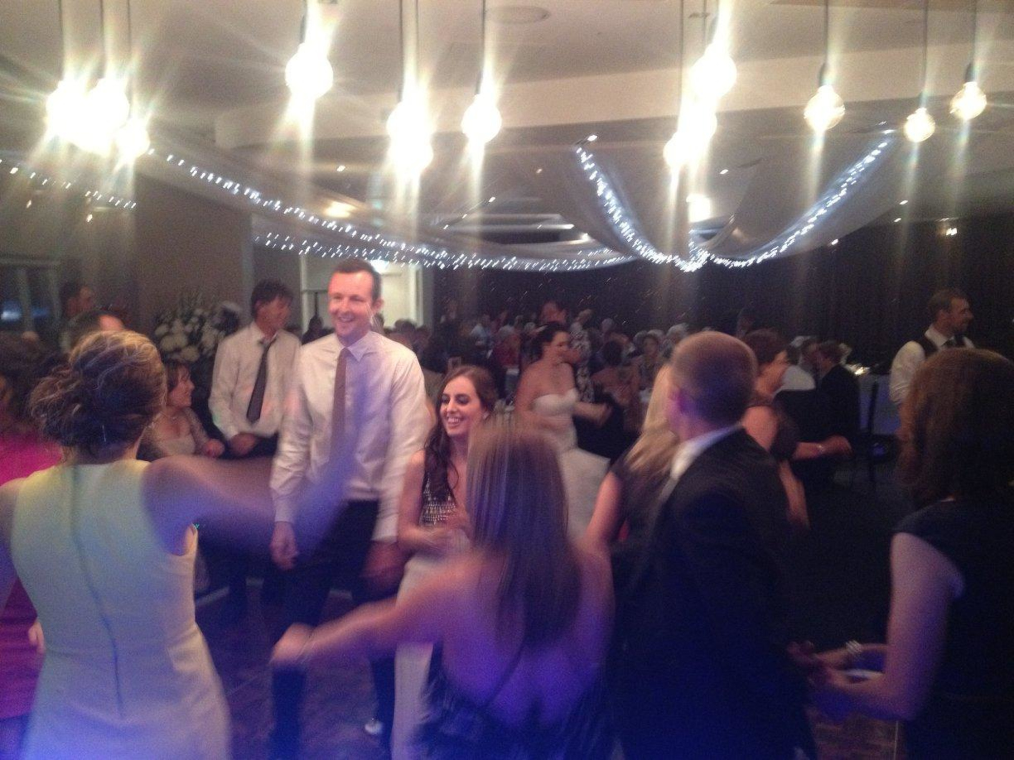 Wedding guests dance together on a lively reception dance floor under warm string lights.