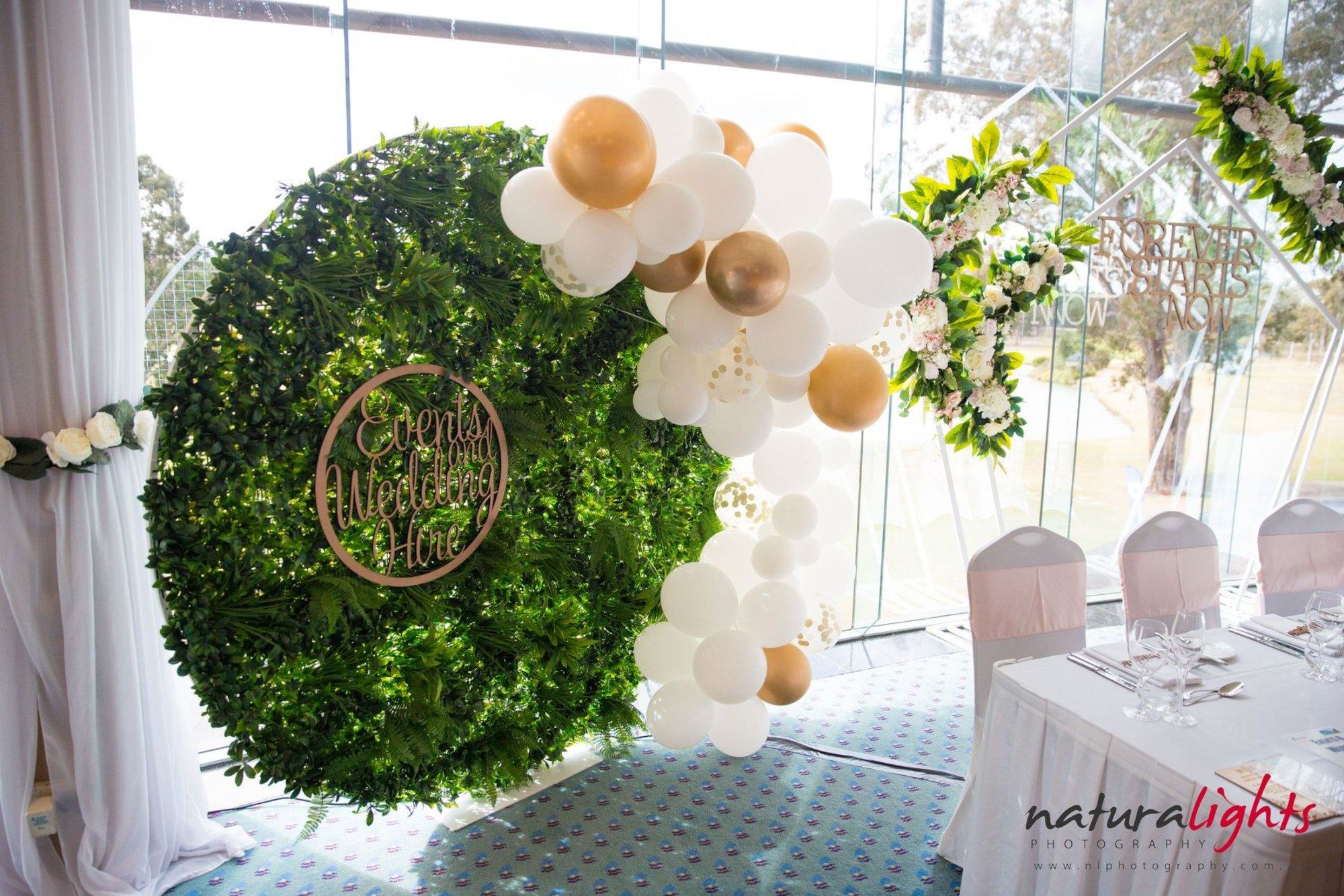 Greenery circle backdrop with white and gold balloon garland beside a decorated wedding reception table.