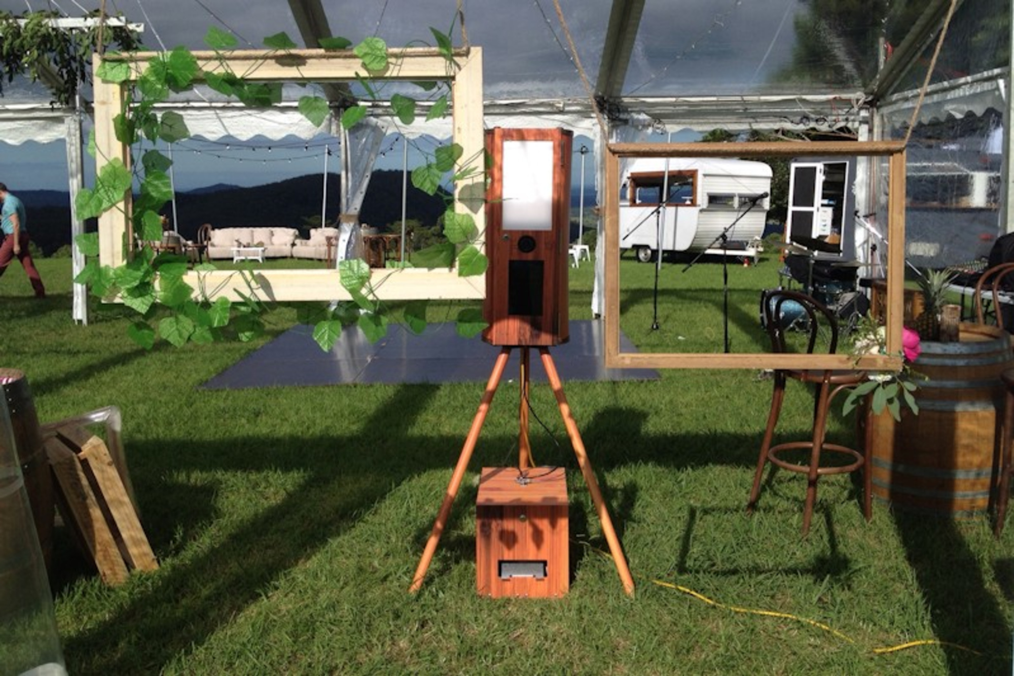 Rustic wooden photo booth with empty frames set up on a grassy outdoor wedding reception lawn.