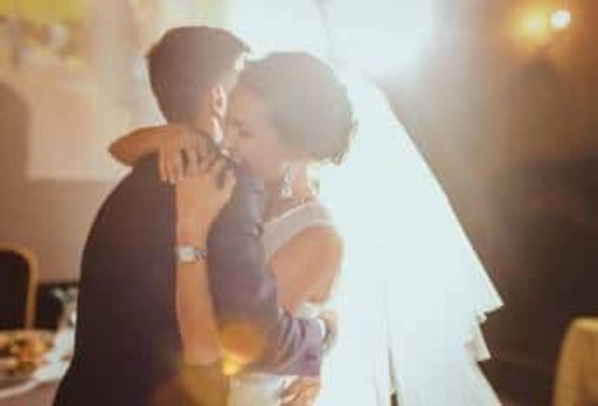 Bride and groom share a romantic first dance in warm backlit lighting at their wedding reception.